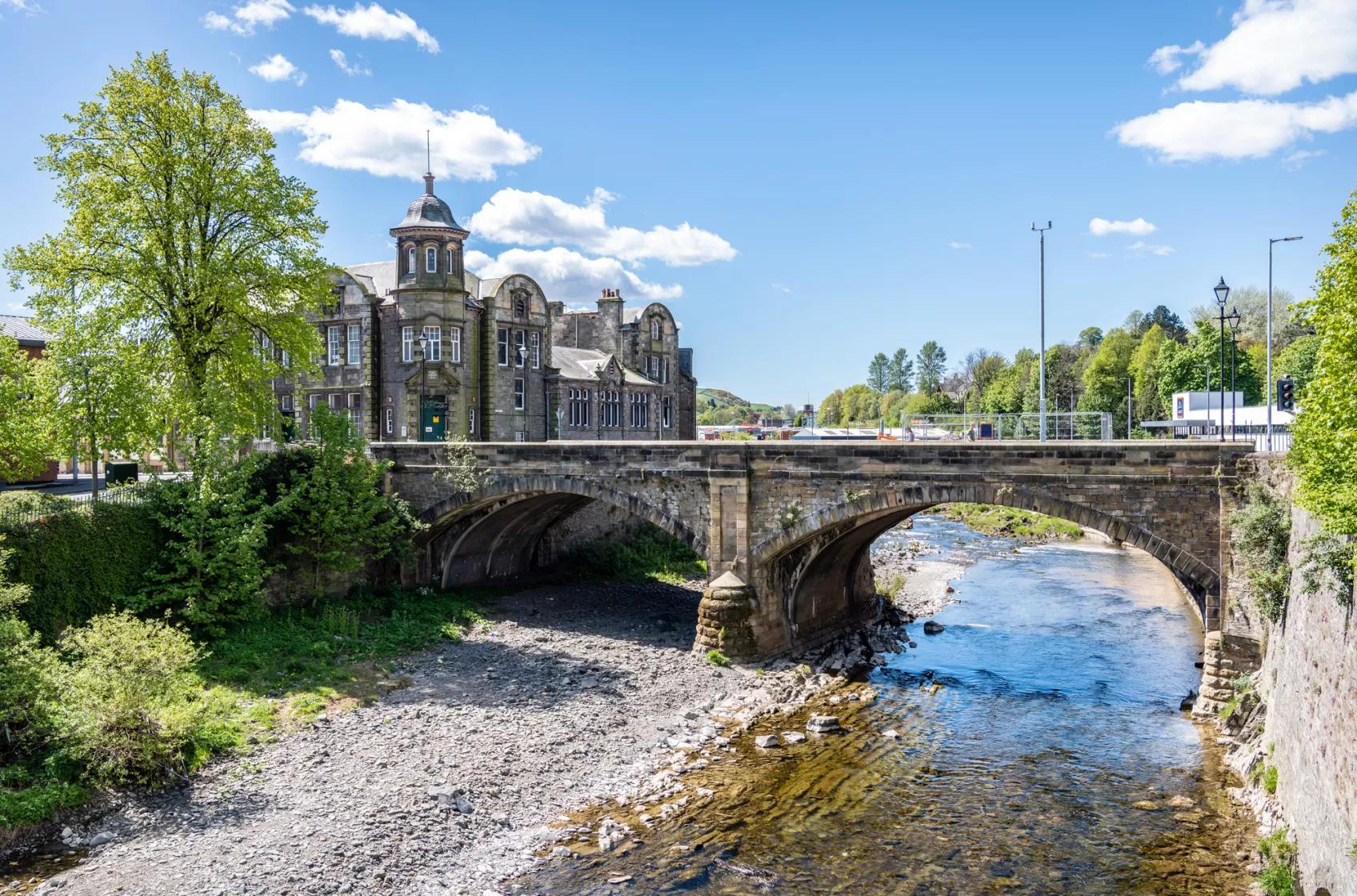 A stone arch bridge over a river in a Scottish border town, with a turreted building behind