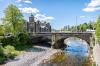 A stone arch bridge over a river in a Scottish border town, with a turreted building behind