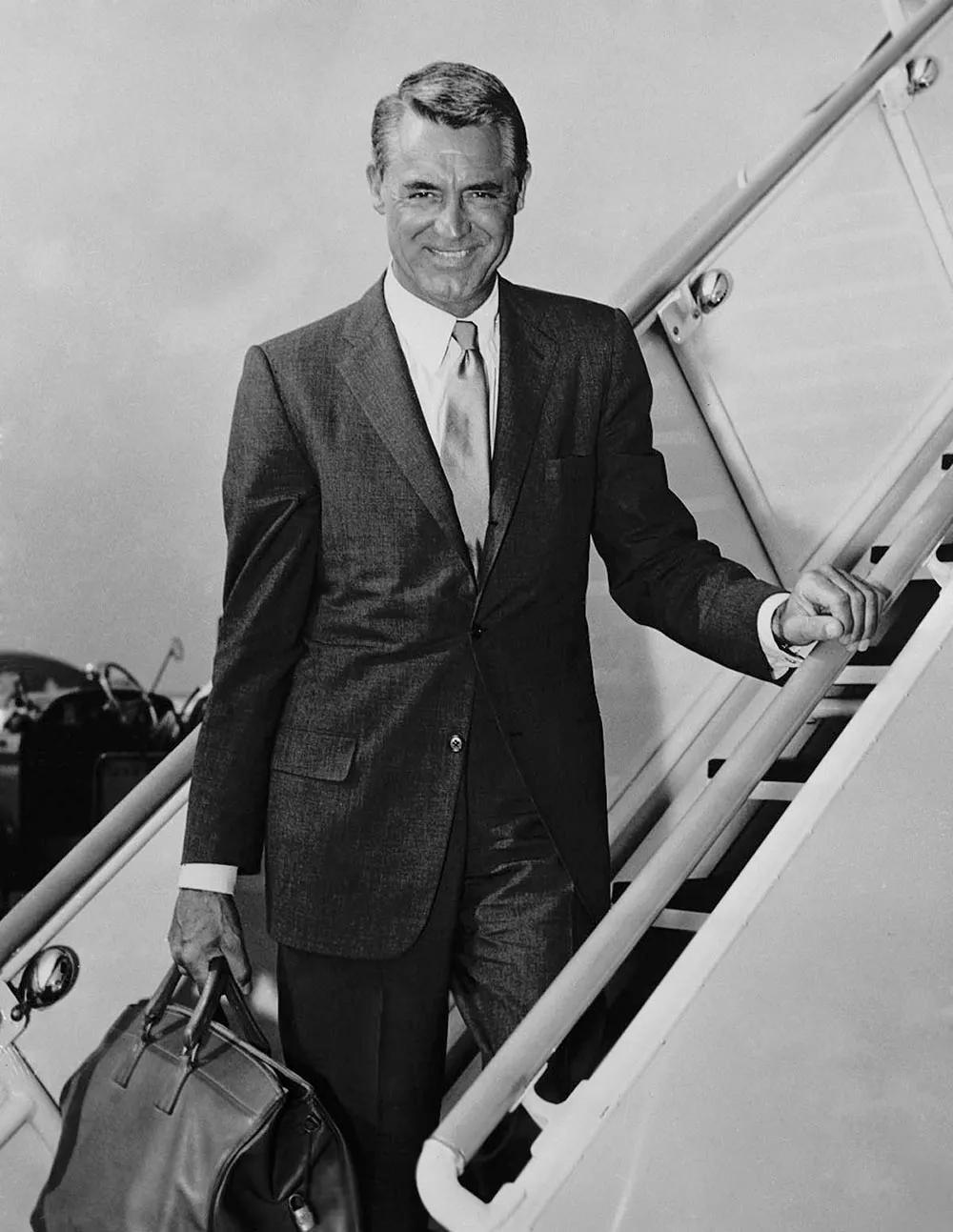 Cary Grant in a suit boarding a plane, carrying a leather duffle bag
