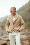A man in a cream shawl-collar cardigan and white trousers in a hillside valley