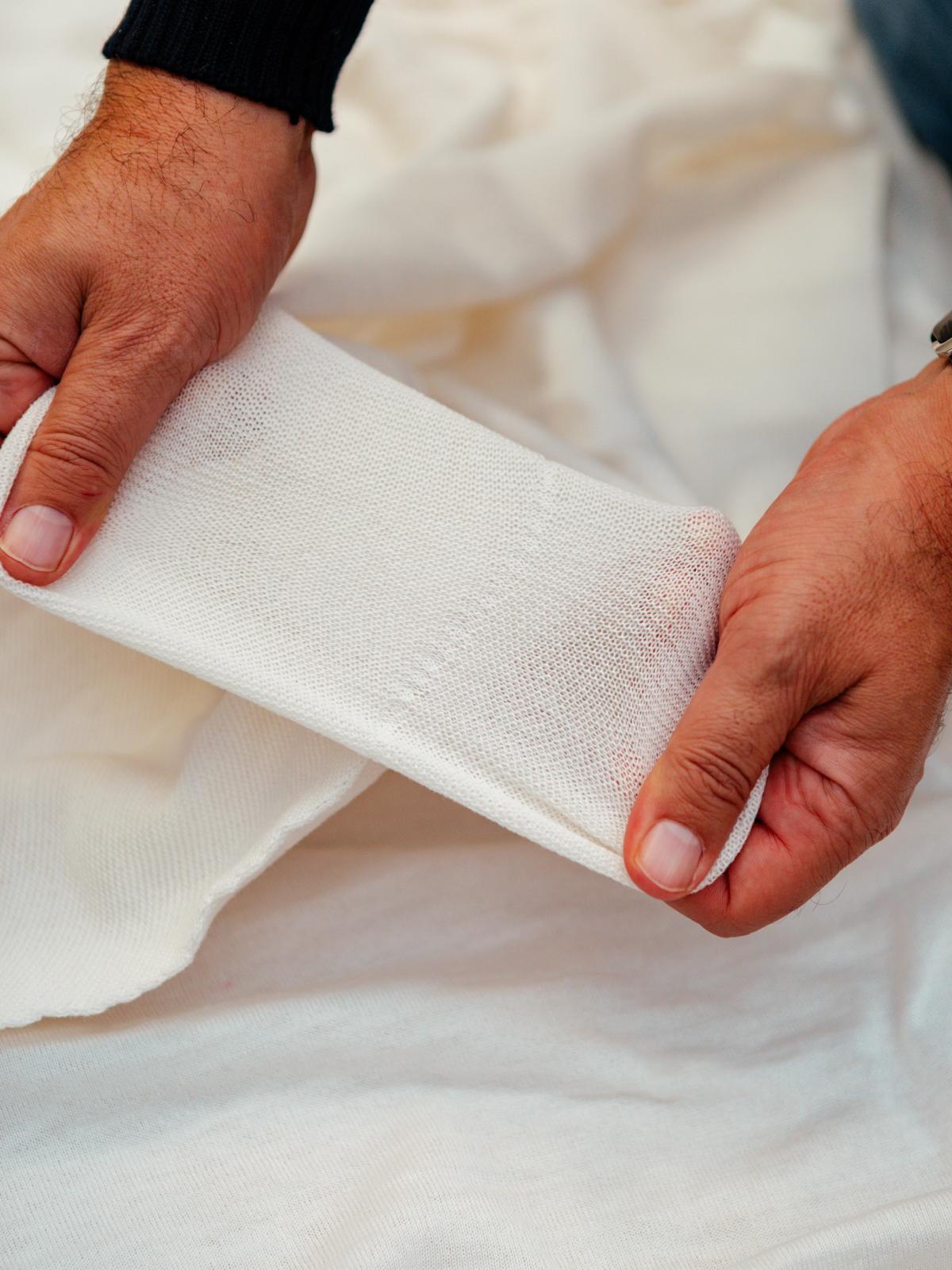 Hands inspecting a panel of white knitted fabric
