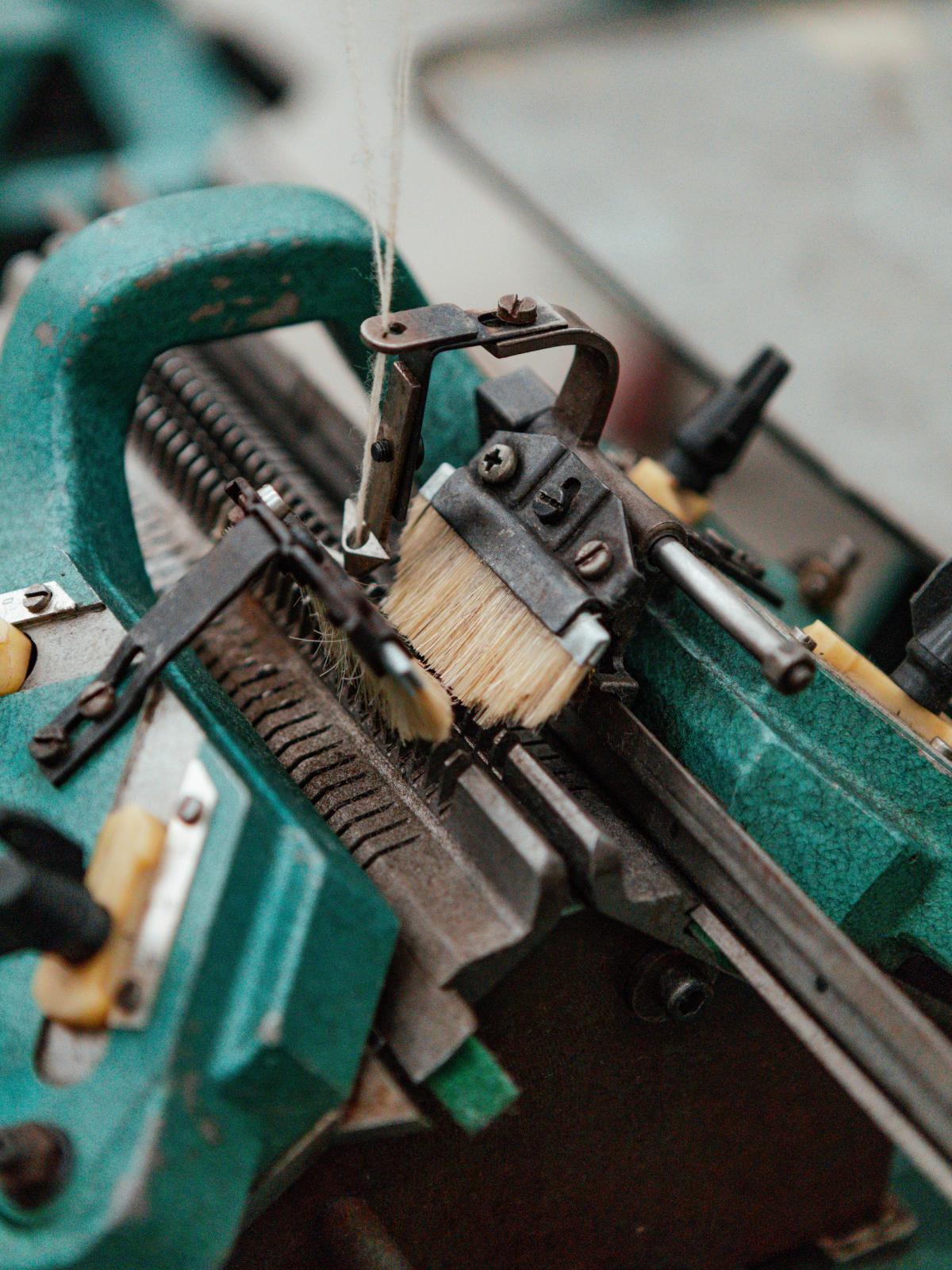 Close-up of the needle bed of a green industrial knitting machine