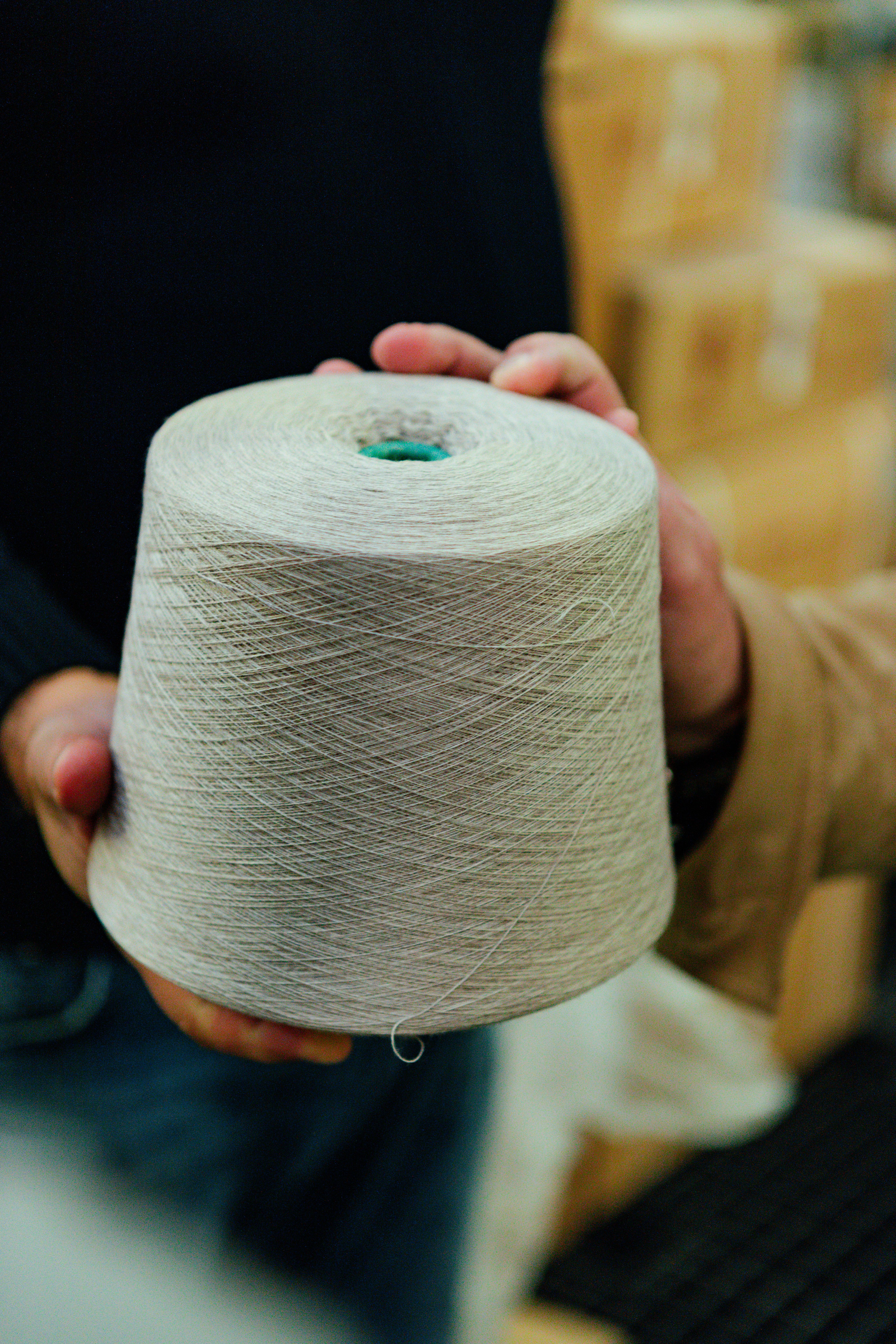 Hands holding a cone of undyed cream yarn