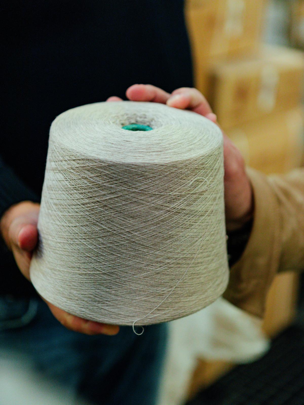 Hands holding a cone of undyed cream yarn