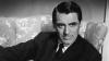 Cary Grant in a dark pinstripe suit seated on a floral sofa