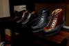 Black and brown leather boots and shoes displayed on a dark wooden shelf