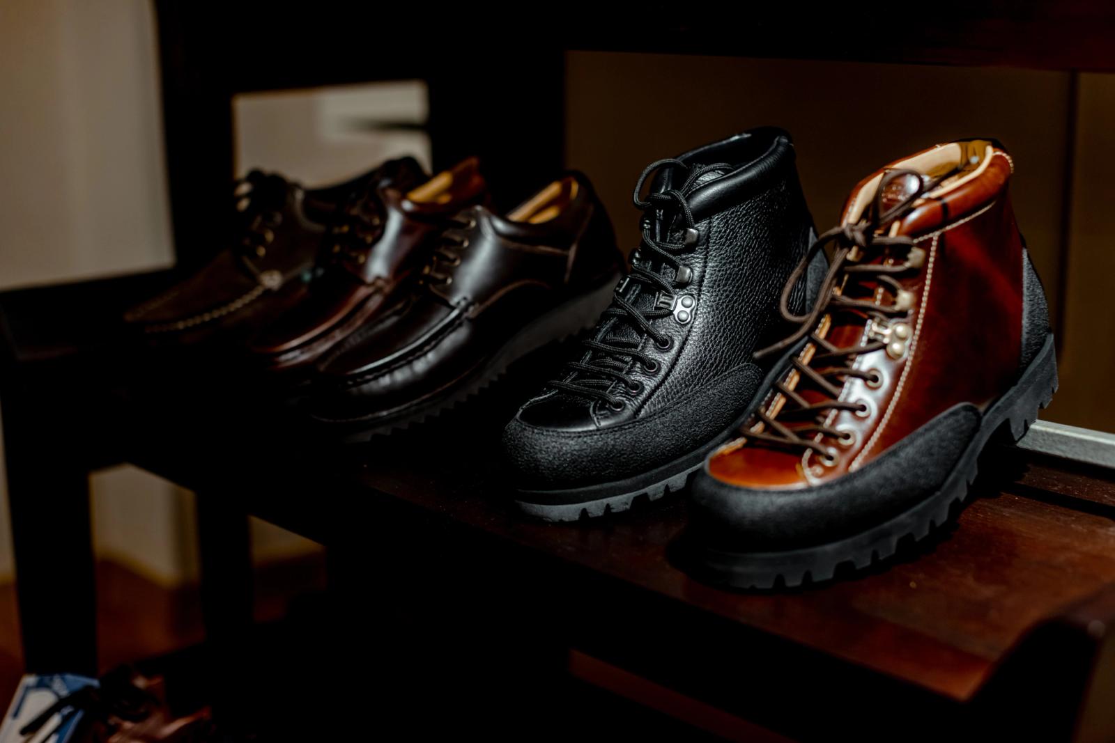 Black and brown leather boots and shoes displayed on a dark wooden shelf