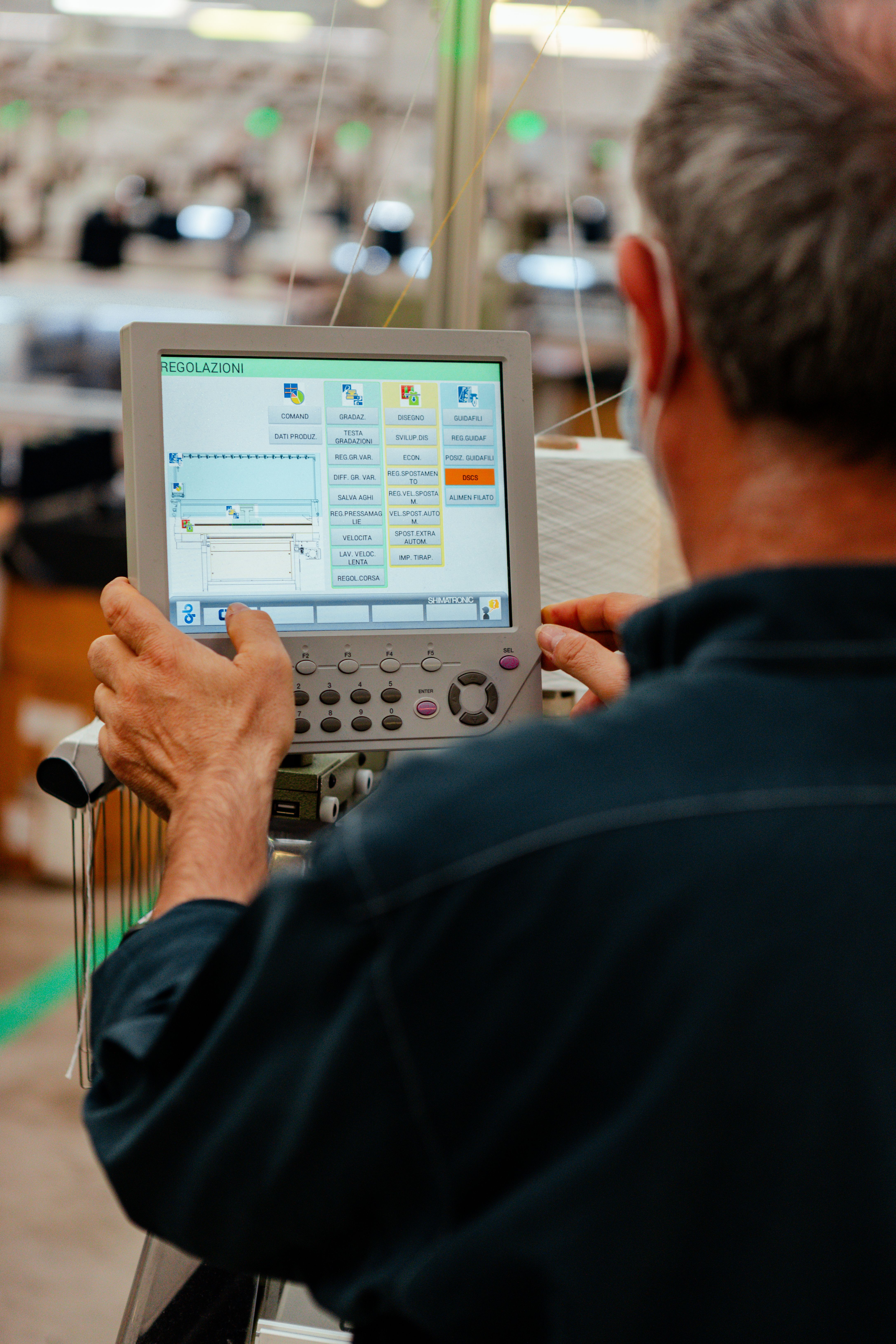 A technician operating the control panel of an industrial knitting machine