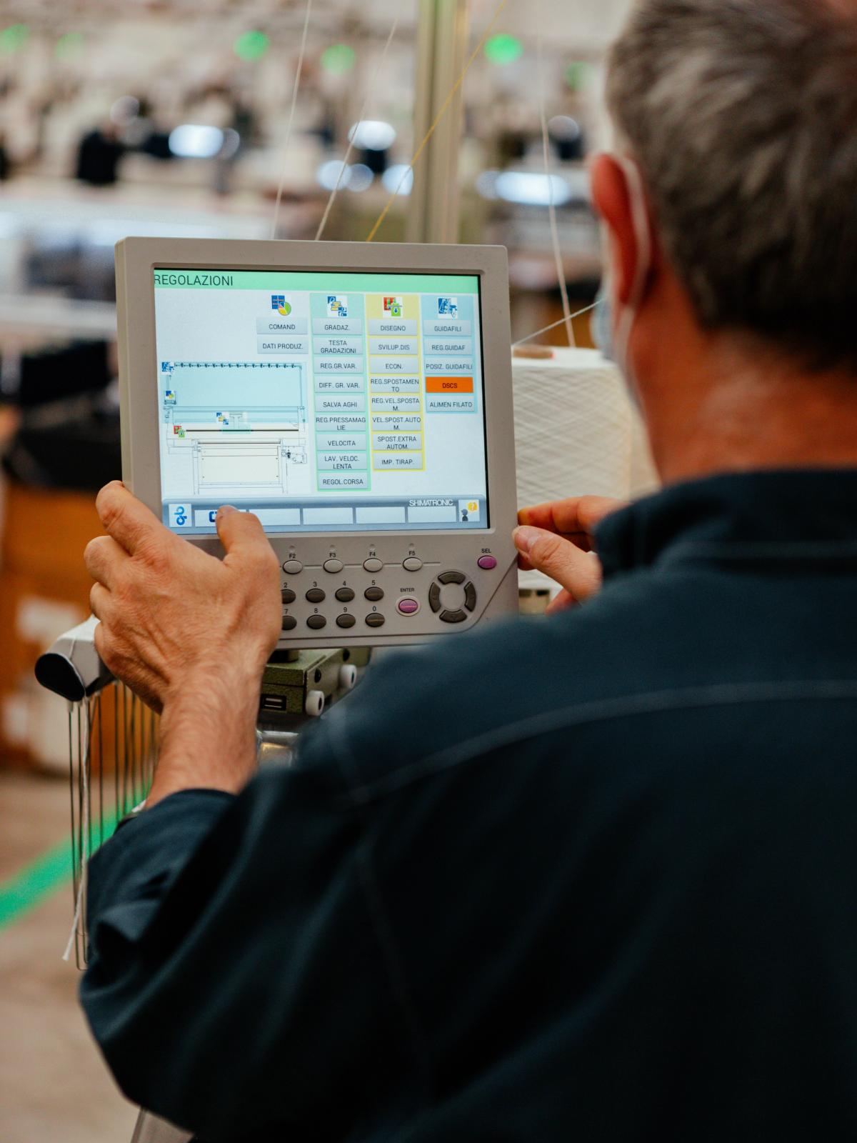 A technician operating the control panel of an industrial knitting machine