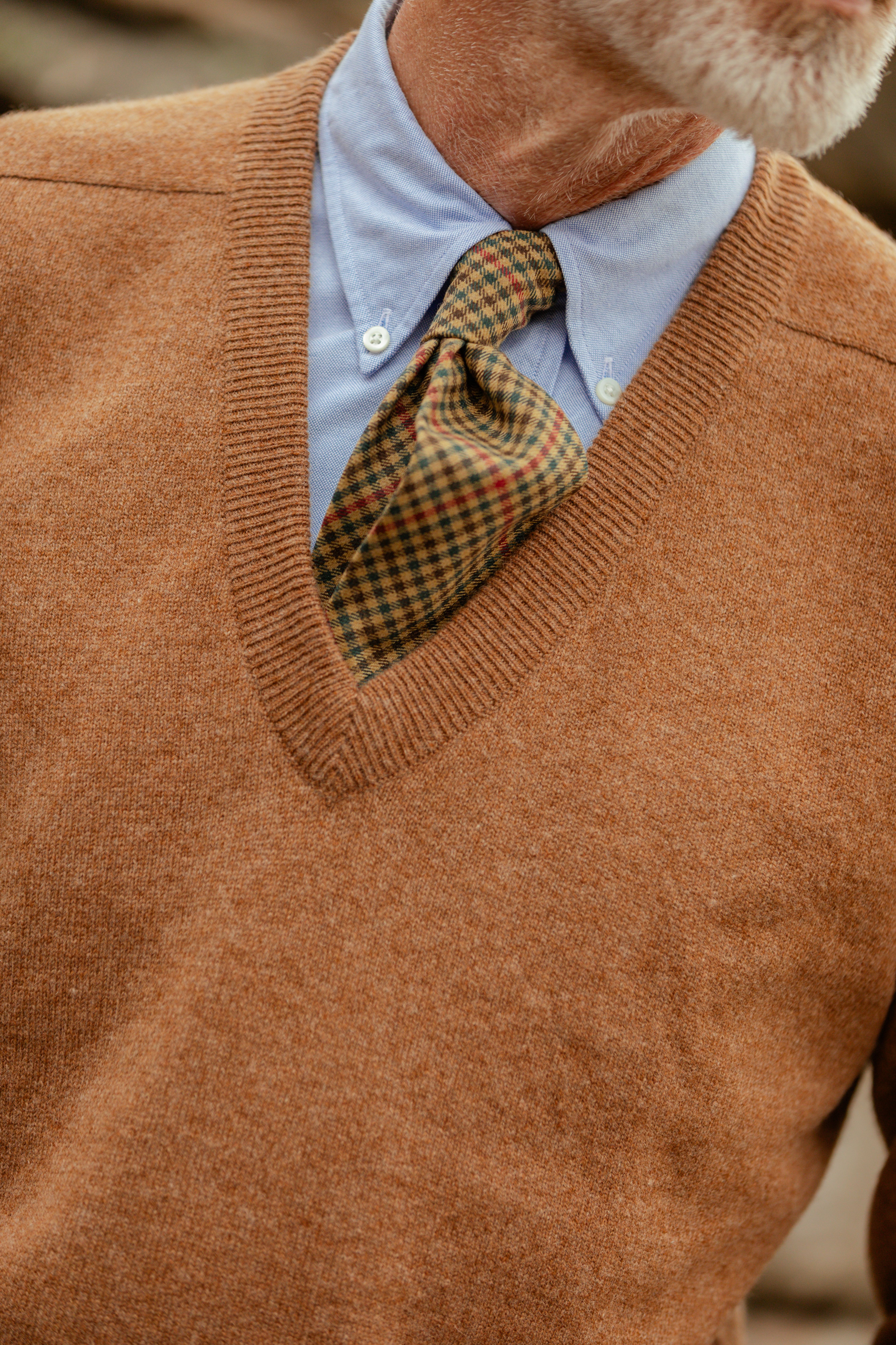 Close-up of a rust-coloured V-neck sweater worn over a shirt and patterned tie
