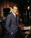 Cary Grant in a grey suit on a film set, beside a director's chair marked Hitchcock