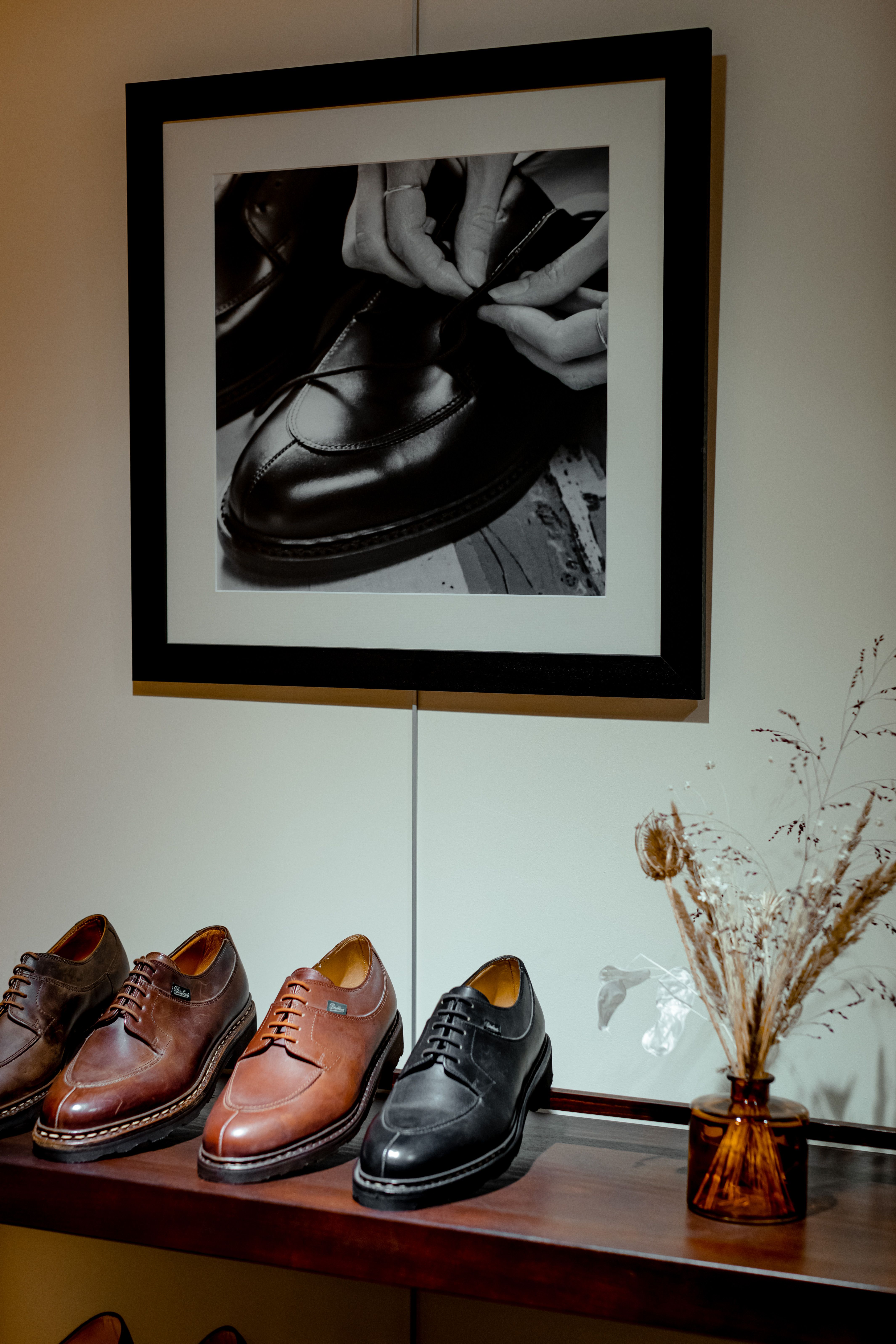 A shop display shelf of leather shoes beneath a framed black-and-white photograph