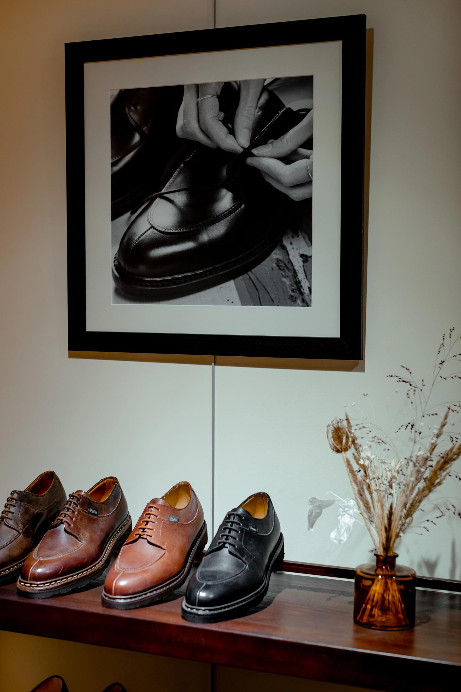 A shop display shelf of leather shoes beneath a framed black-and-white photograph