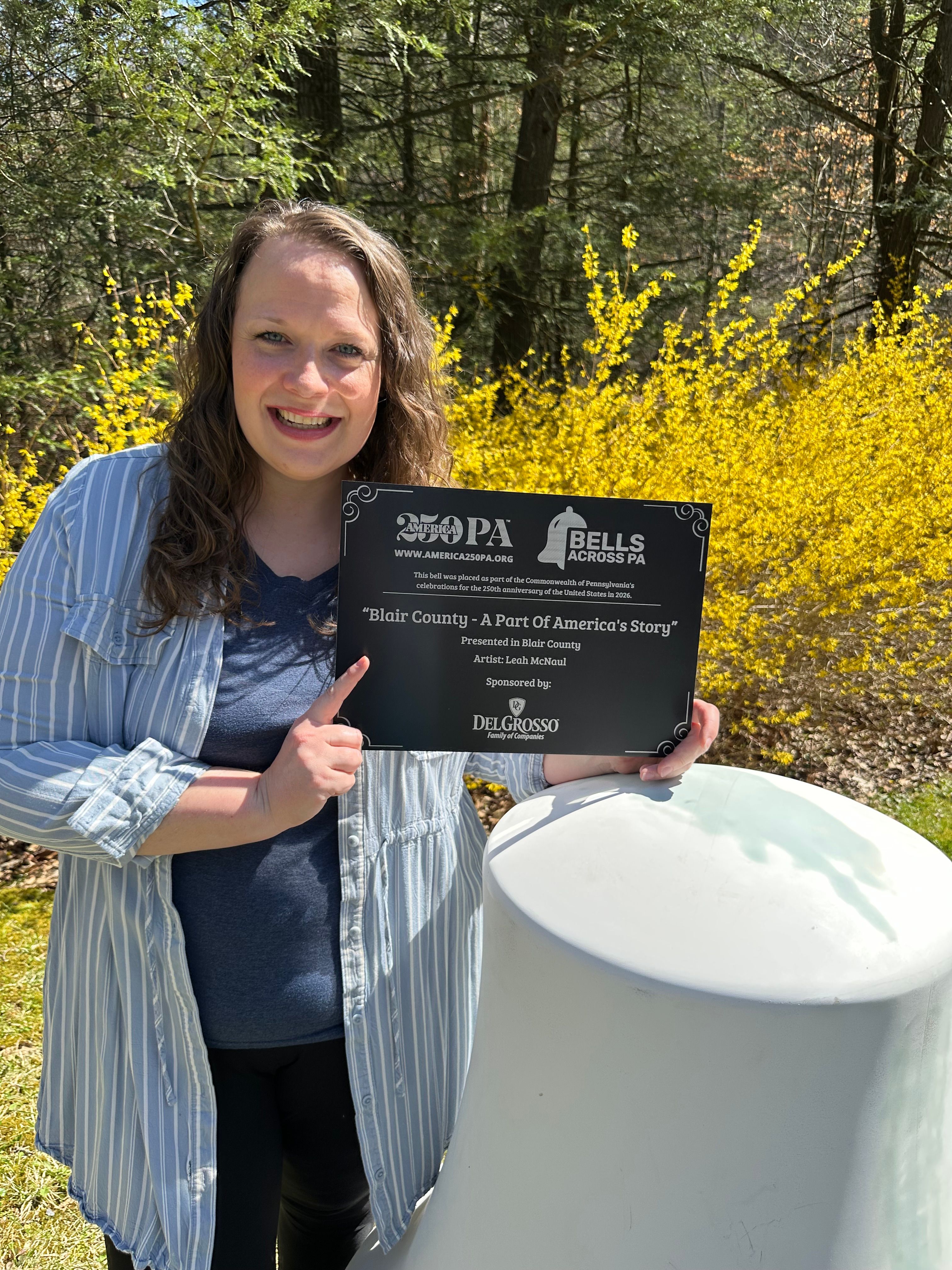 Artist Leah McNaul holding 250 PA Plaque with blank bell in front.