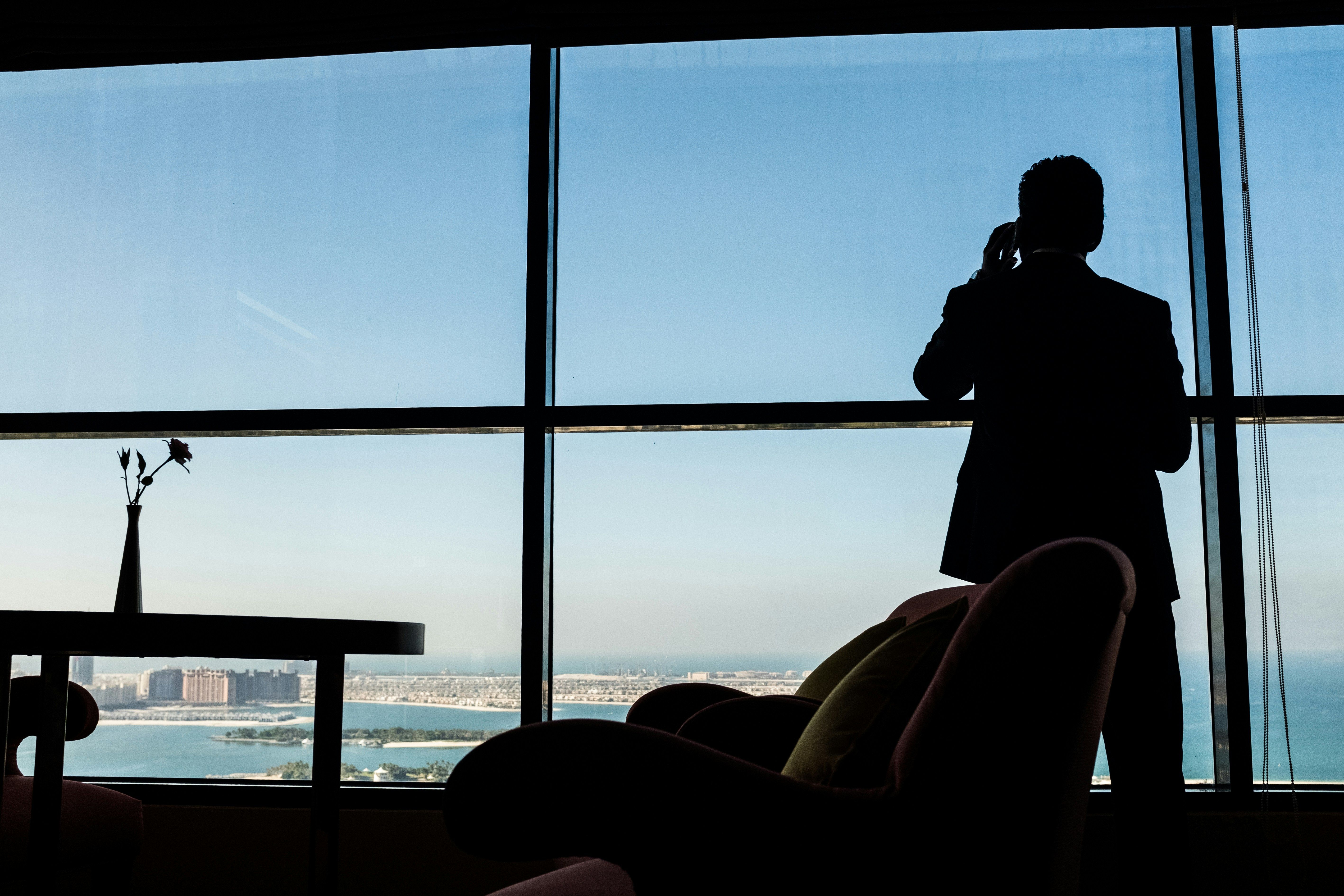 Man looking out a window overlooking the coast while talking on his phone