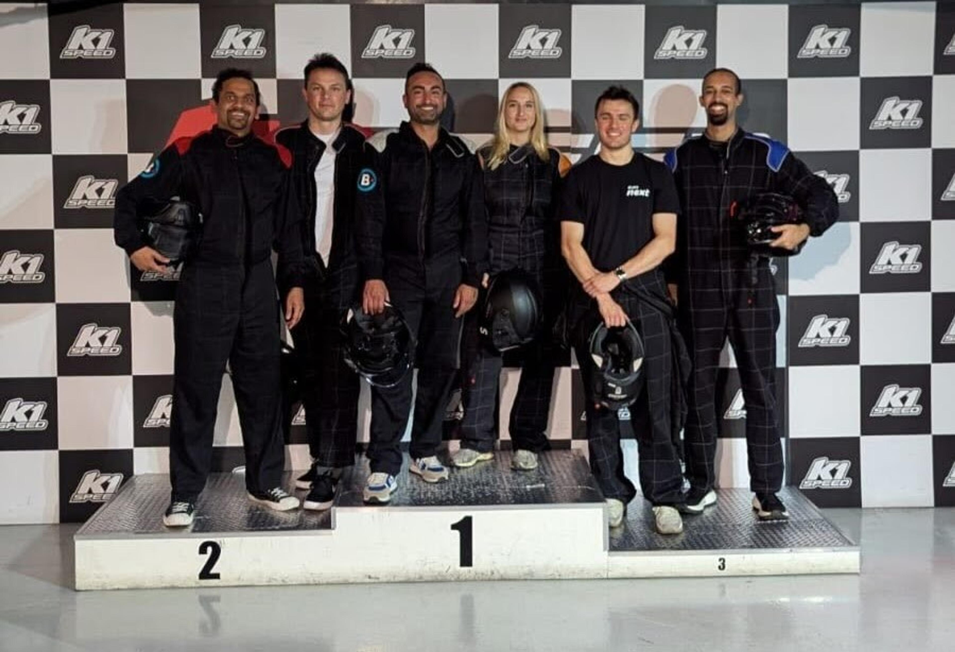 Five people in black racing suits and helmets stand on a podium in front of a K1 Speed backdrop.