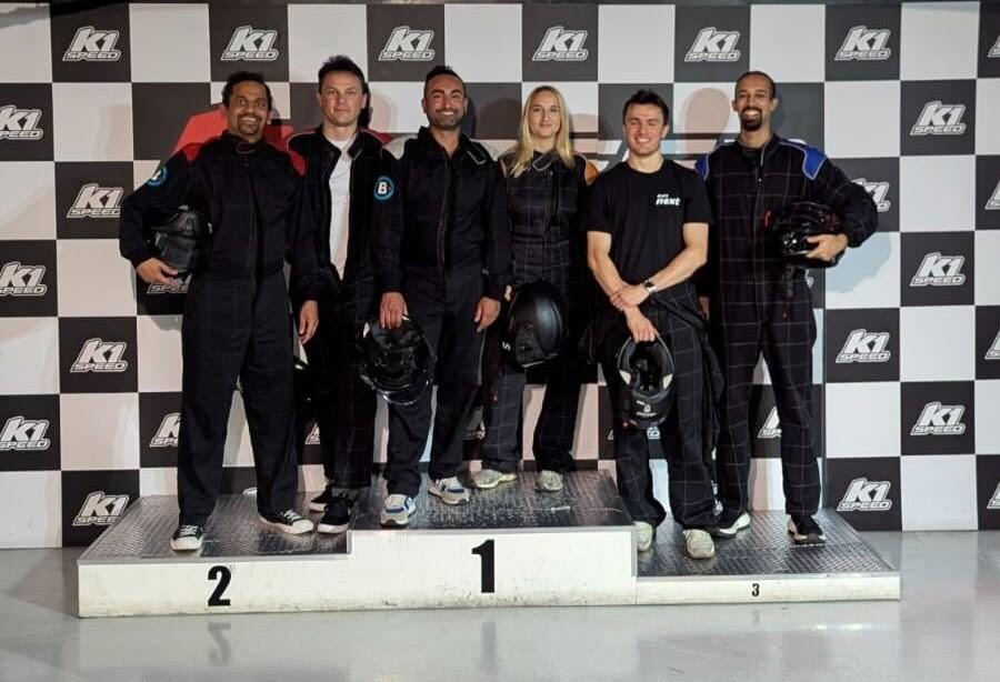 Five people in black racing suits and helmets stand on a podium in front of a K1 Speed backdrop.