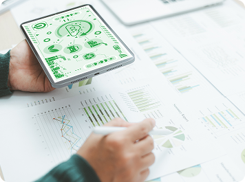 Hand holding a tablet showing sustainability charts over printed reports