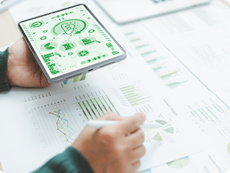 Hand holding a tablet showing sustainability charts over printed reports