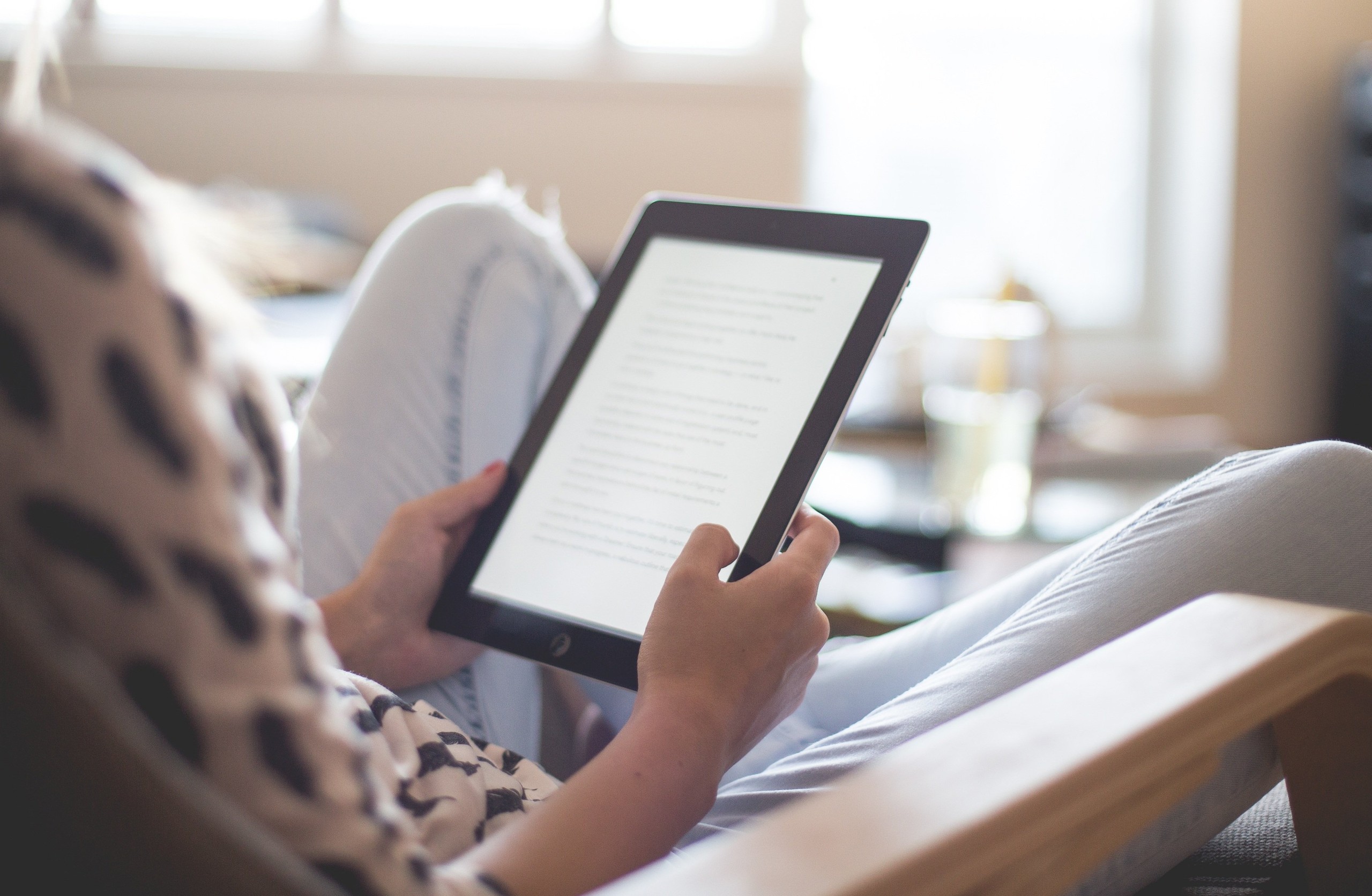 Kvinne som sitter i stol og holder en kindle i hånden.