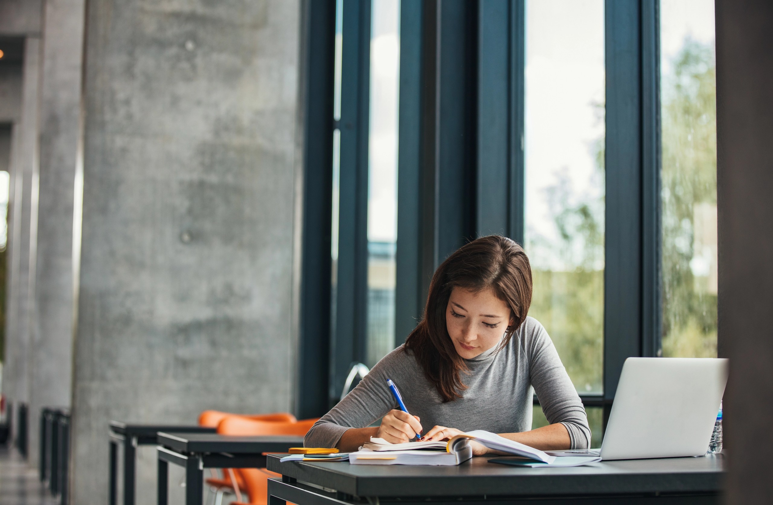 Student på bibliotek som sitter ved en pult og noterer i boka.