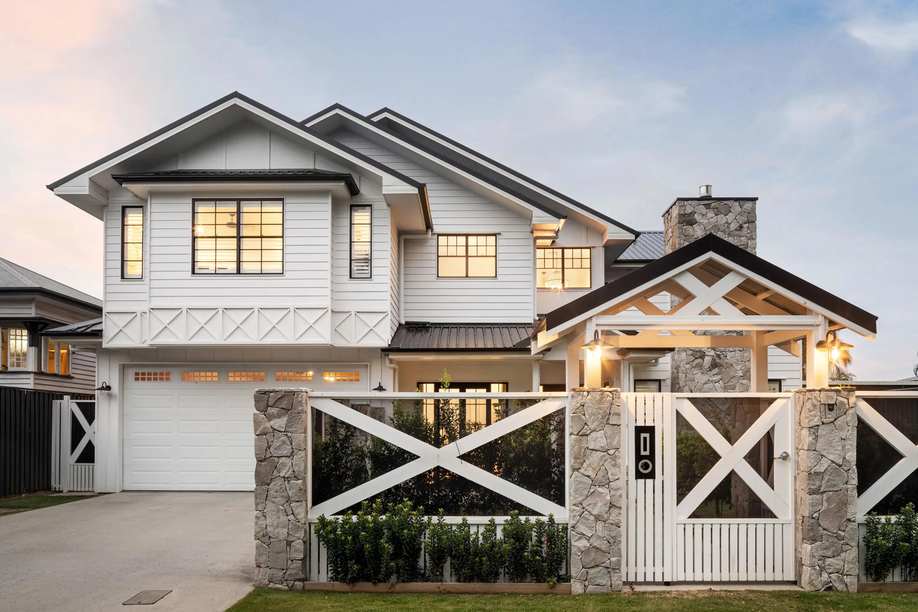 Two storey white weatherboard home with stone gate and garage at dusk