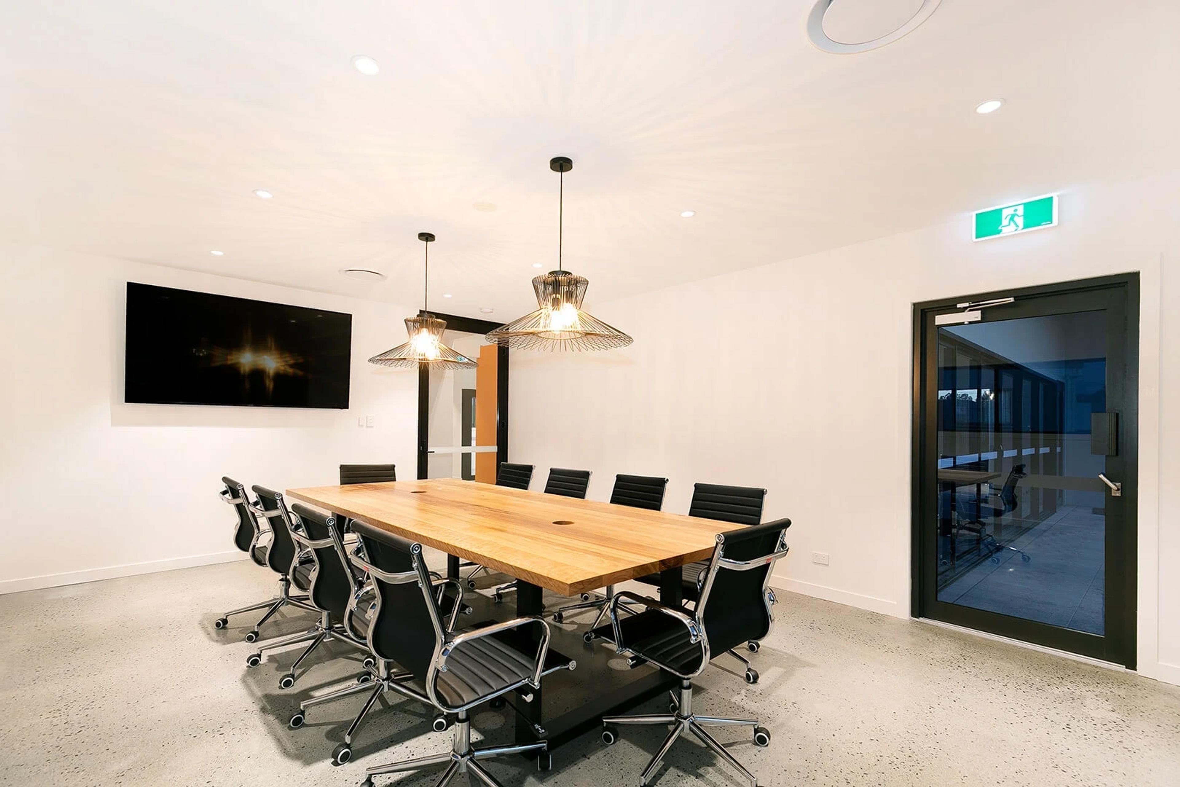 Boardroom with timber table, black chairs and wall screen