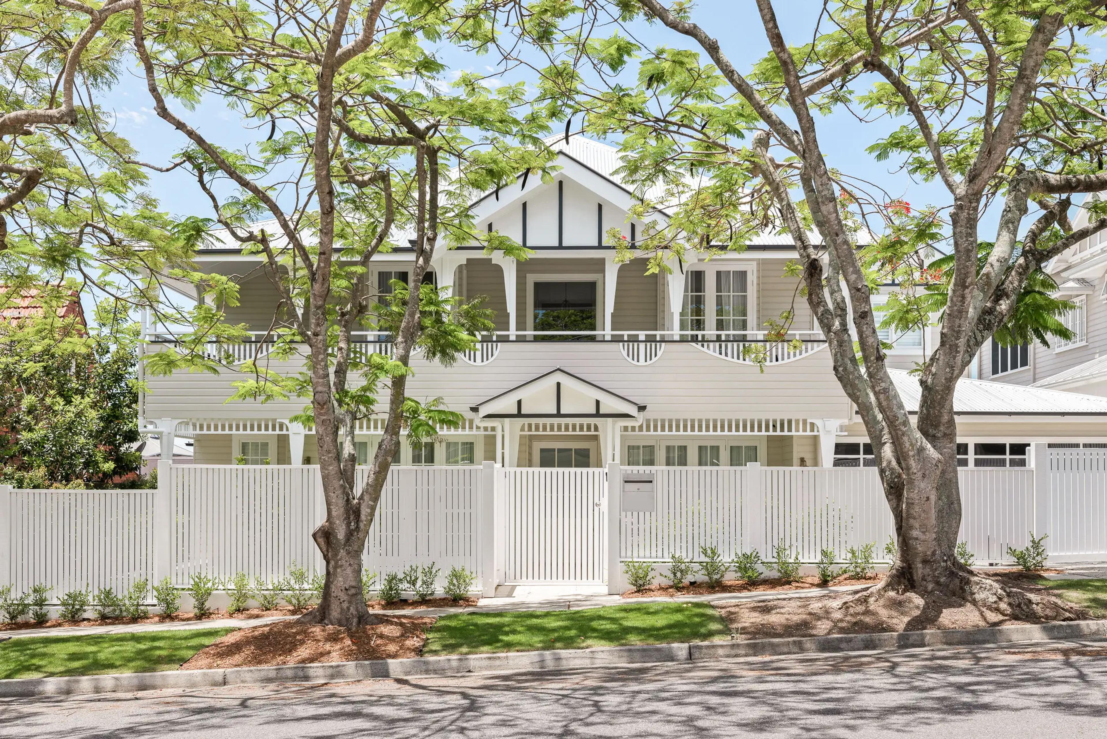 Street facing white weatherboard home behind picket fence and trees