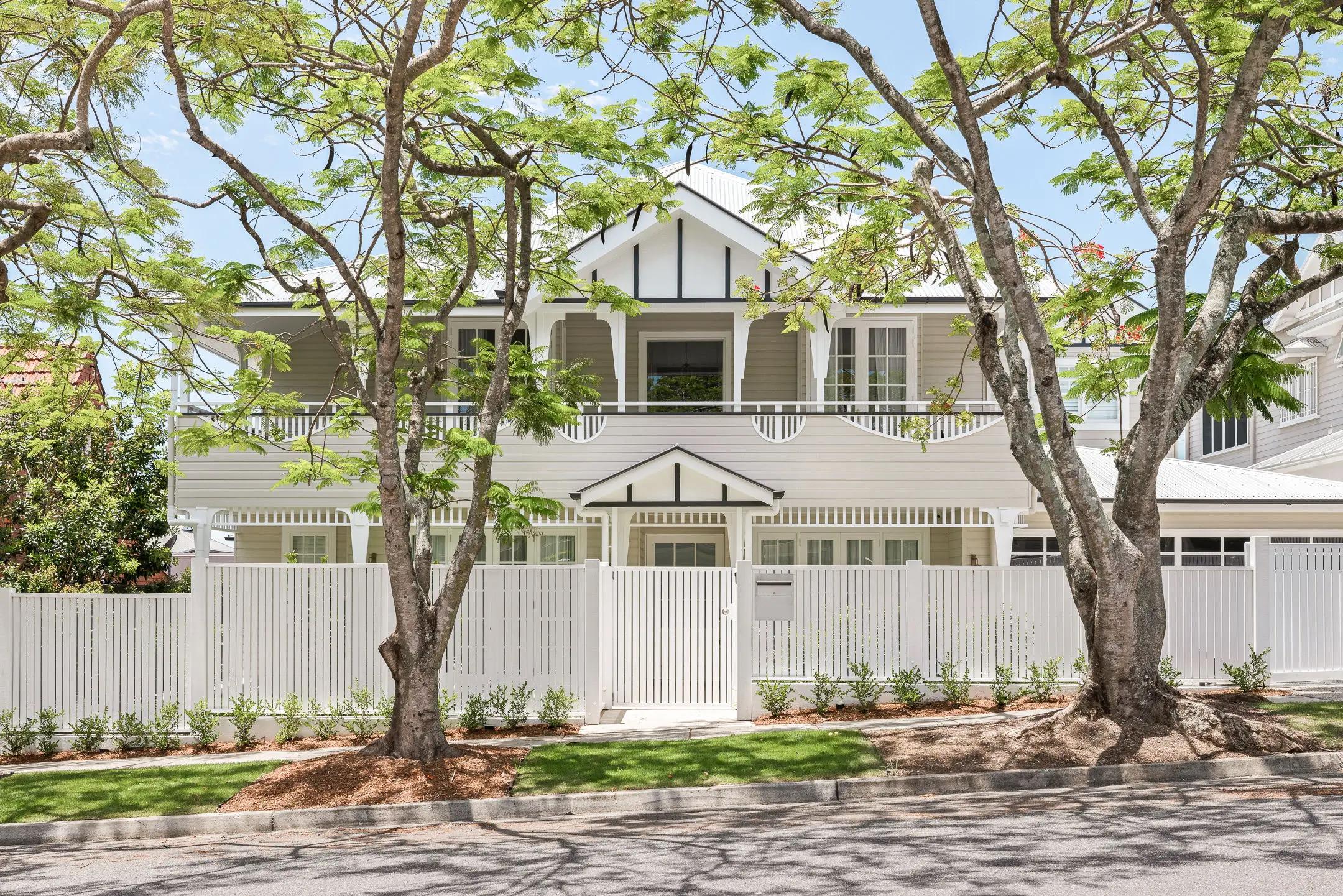 Street facing white weatherboard home behind picket fence and trees