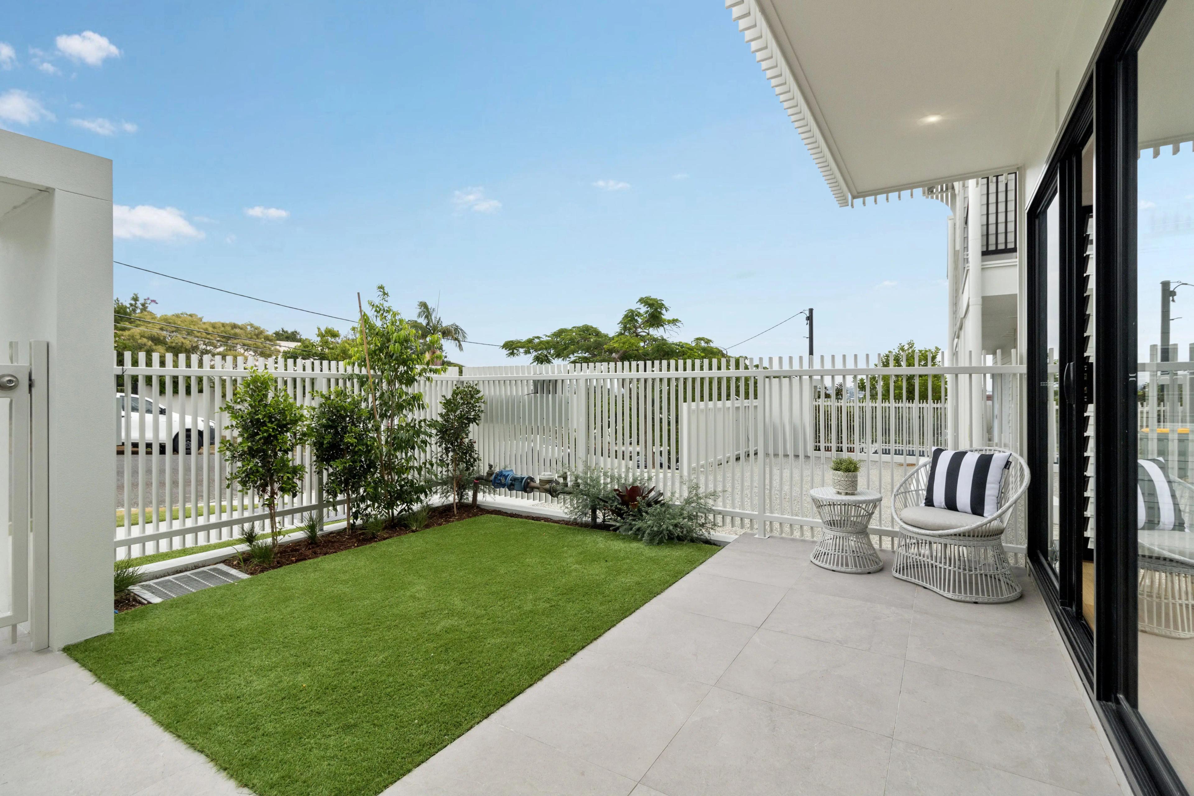 Ground floor courtyard with lawn, white fencing and outdoor chairs