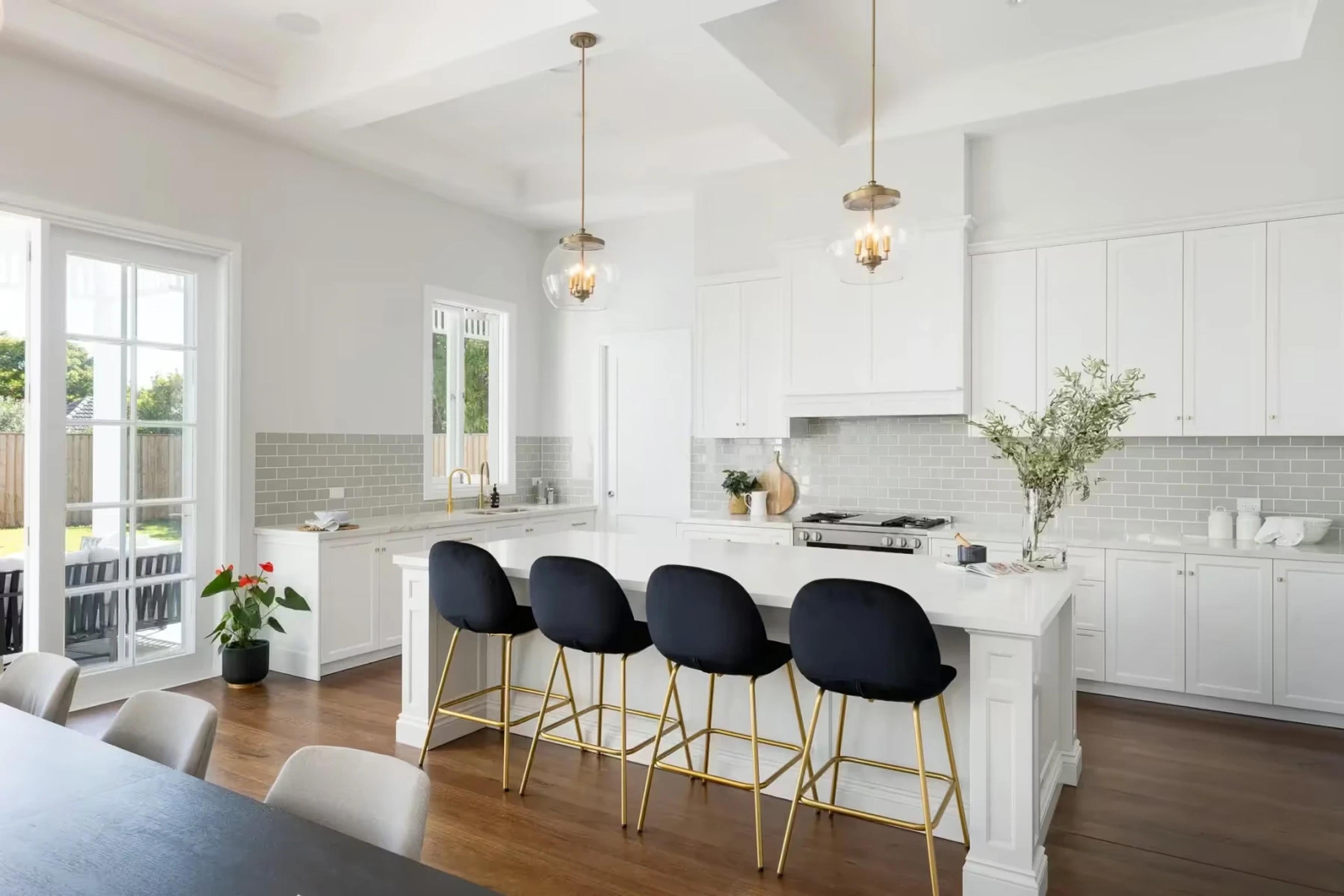 White kitchen with island bench and black bar stools