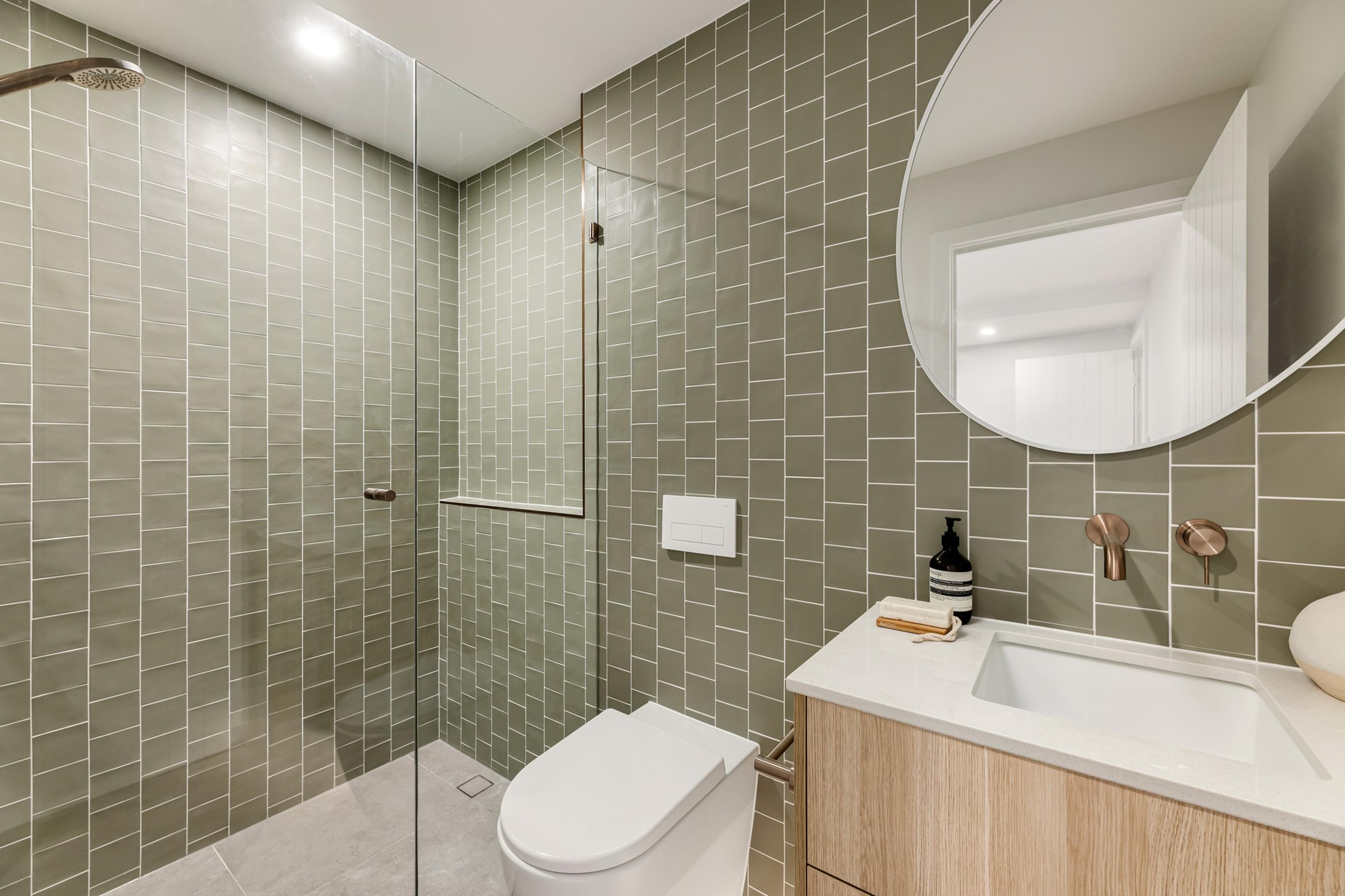 Bathroom with green tiles, timber vanity and round mirror