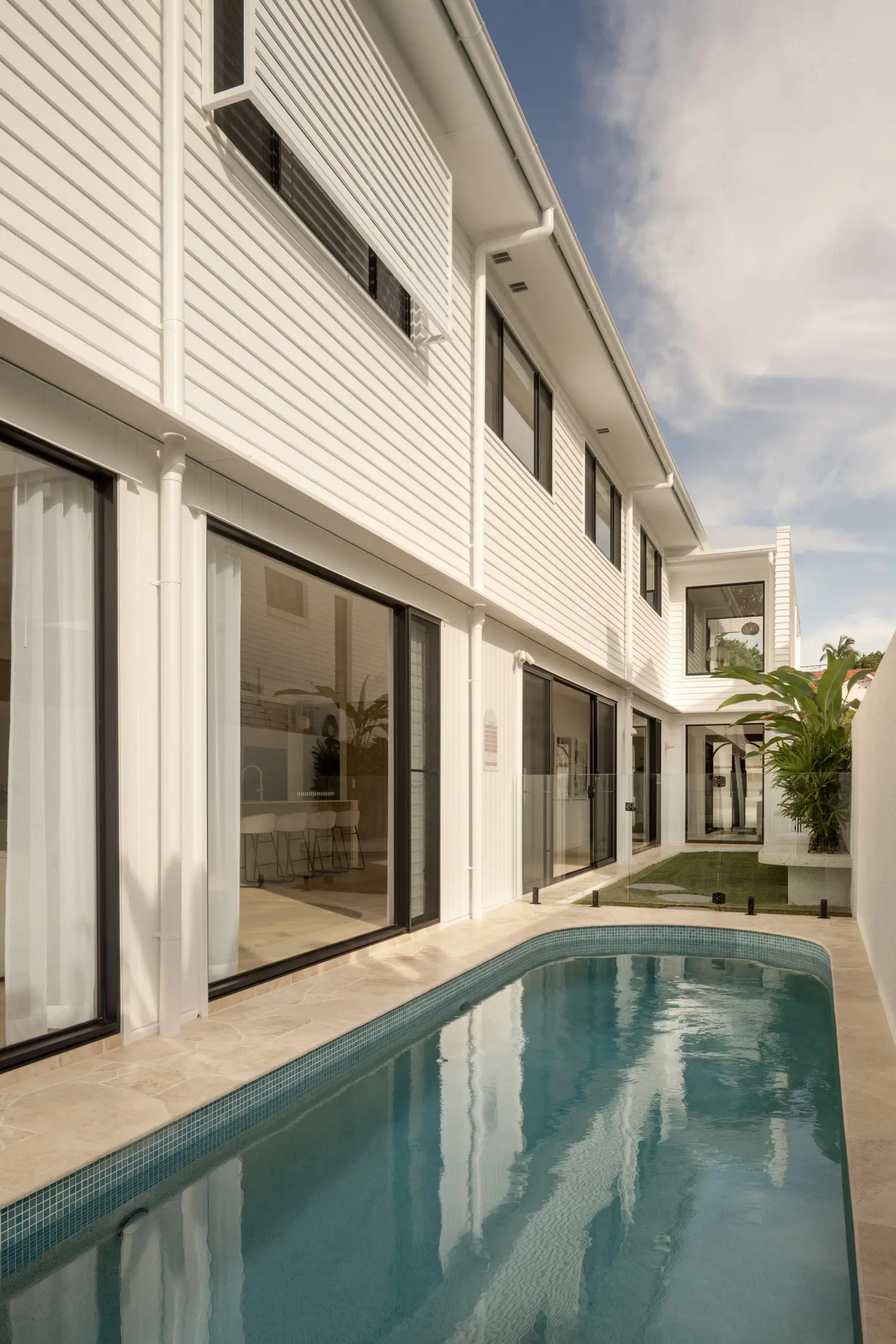 Narrow lap pool alongside white weatherboard home exterior