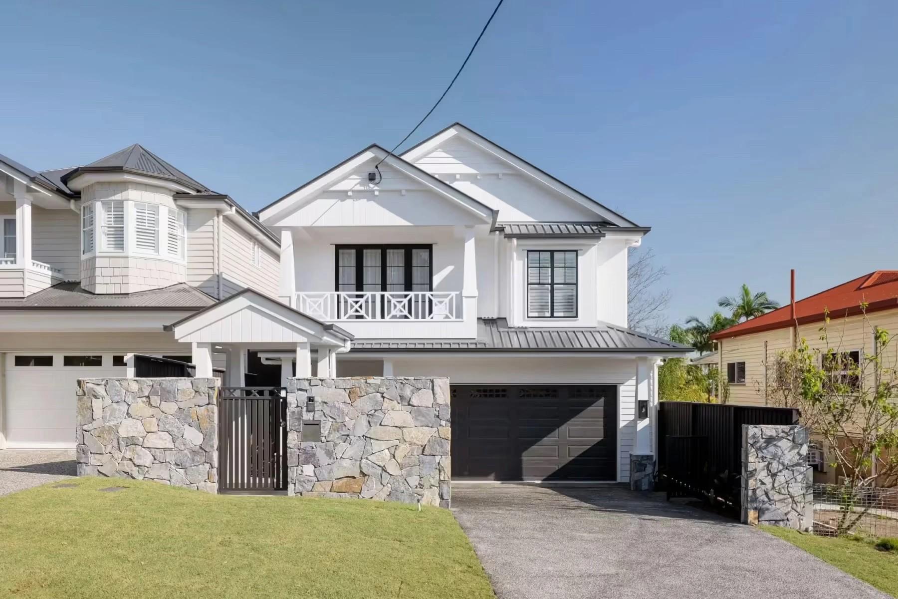Two storey white weatherboard home with stone fence and garage