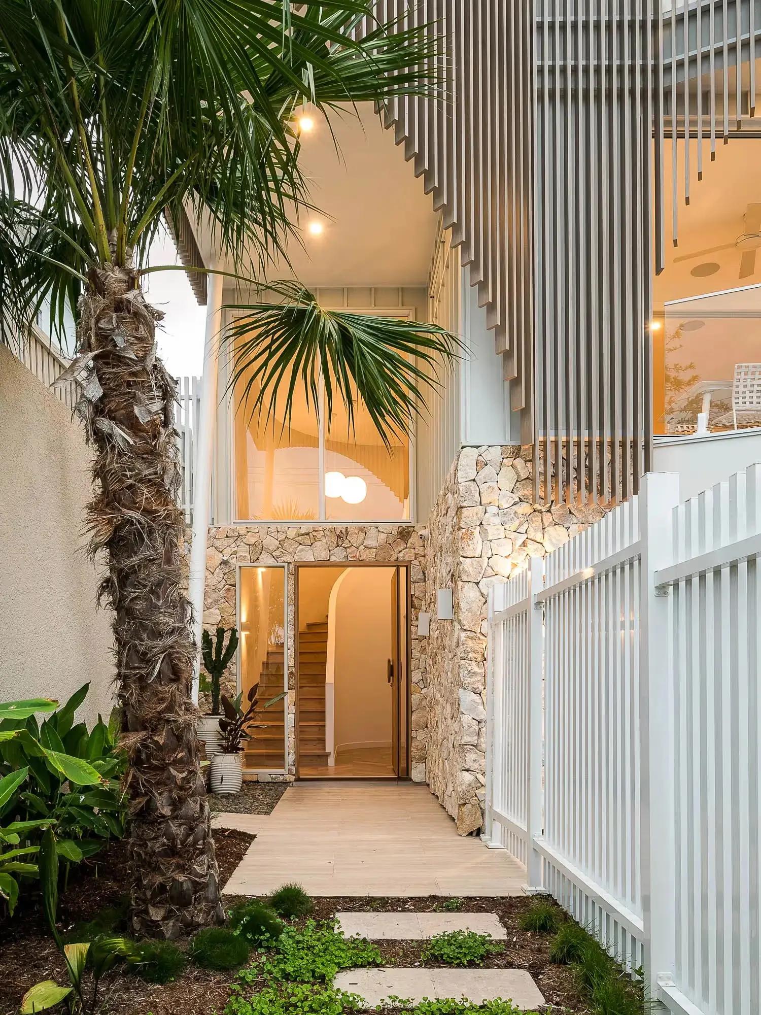 Light-filled modern entryway with a natural stone wall and palm tree landscaping, embodying refined Australian coastal design.