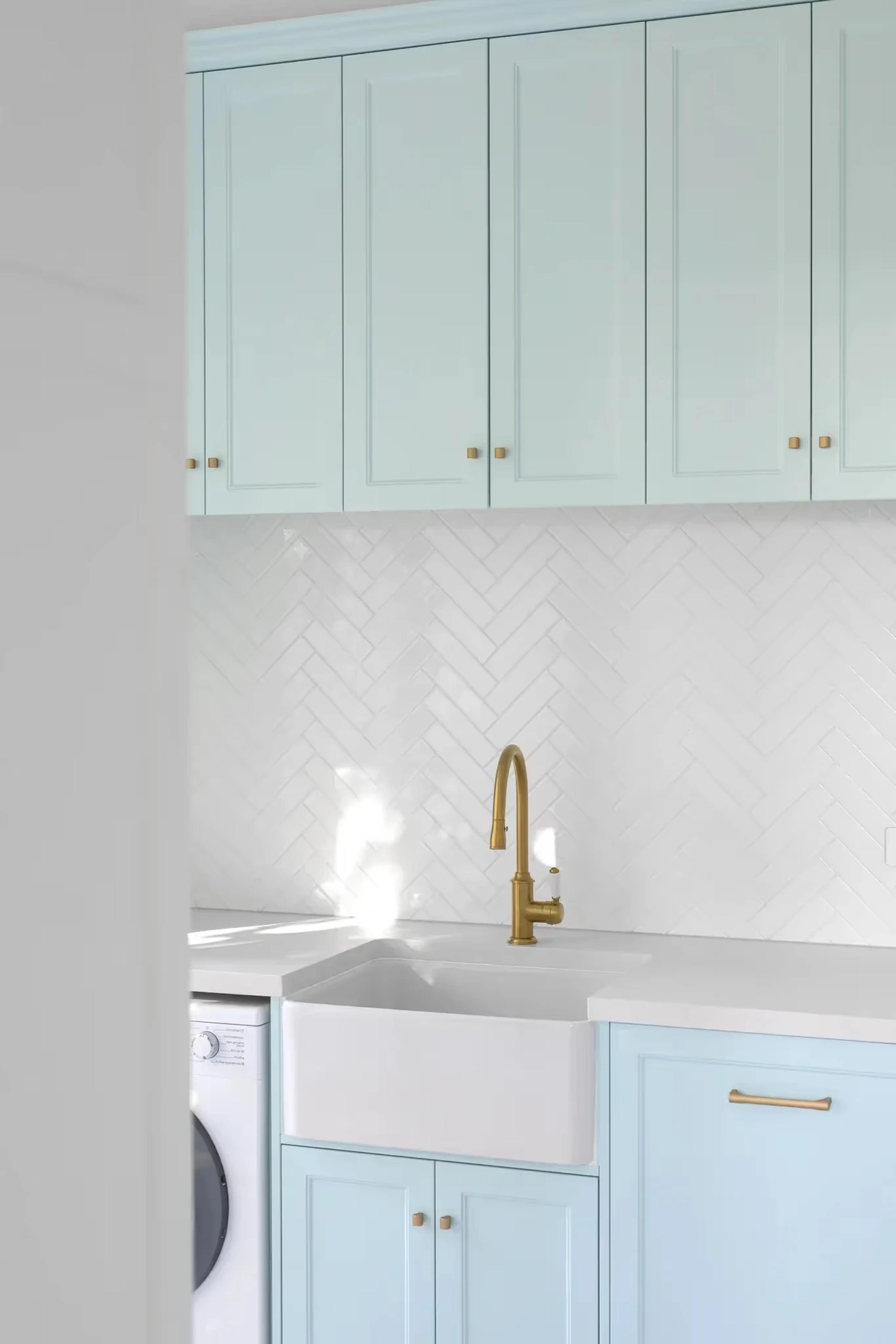Laundry with pale blue cabinetry and gold tapware
