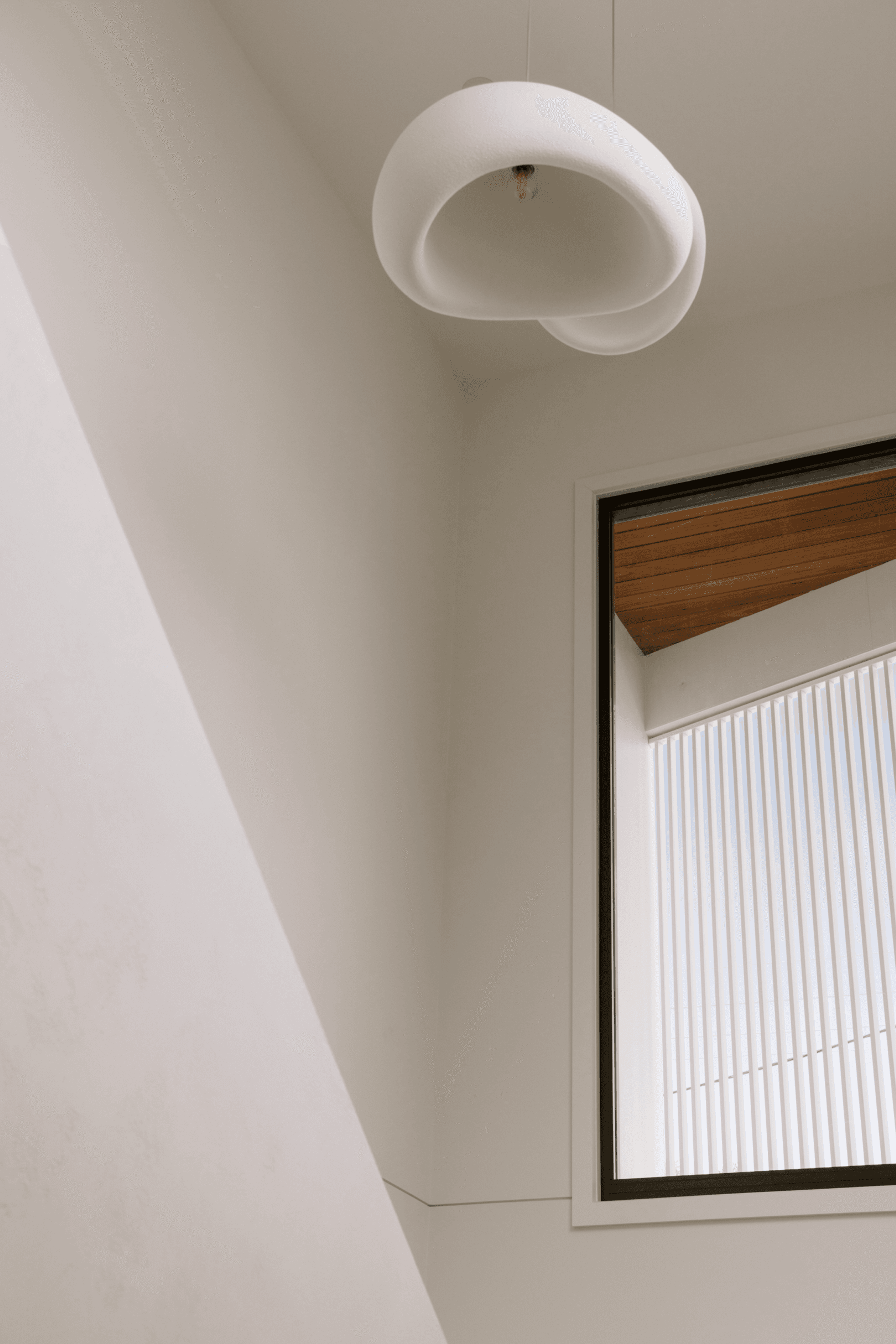 Sculptural pendant light beside window over stairwell