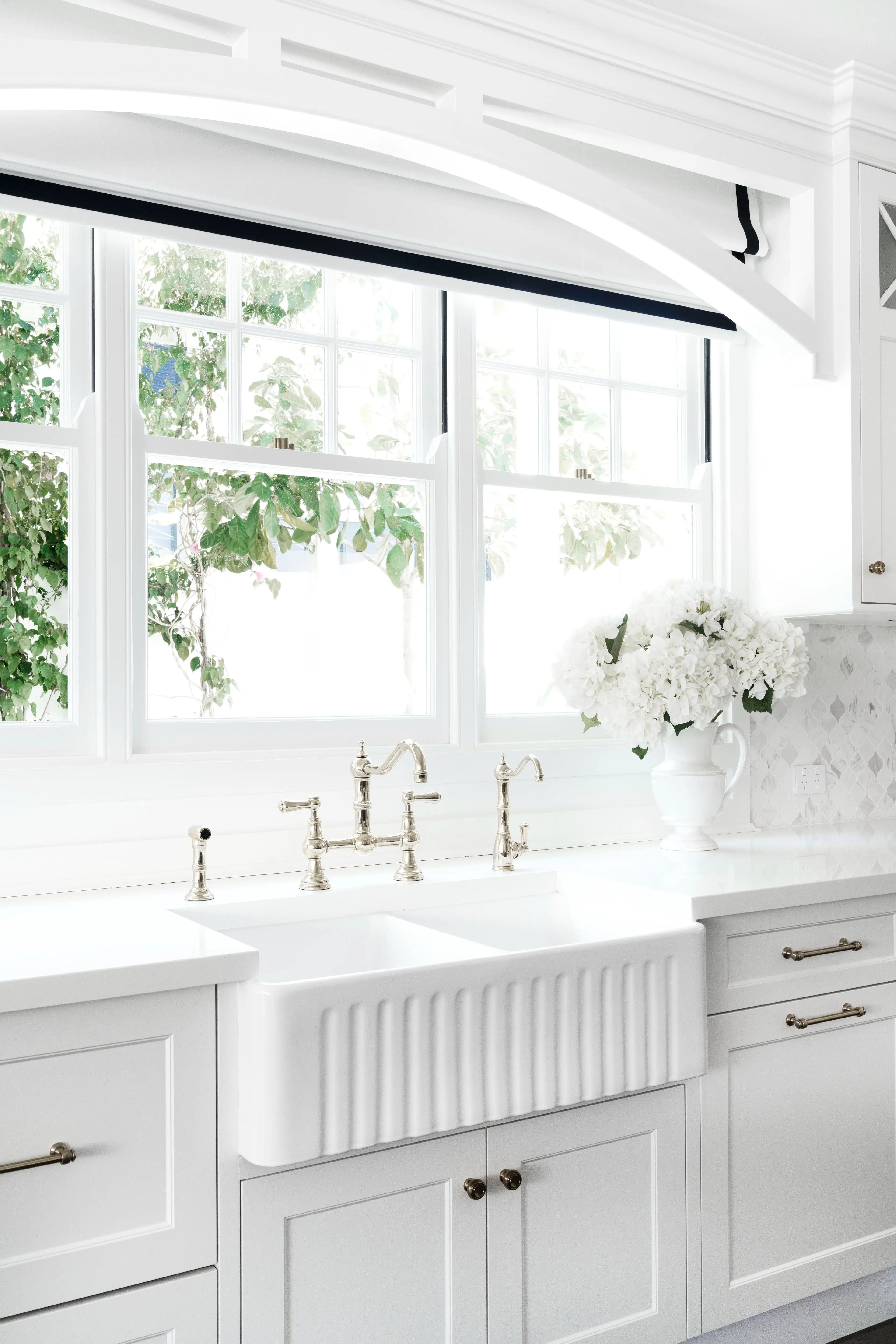 White kitchen with fluted farmhouse sink beneath arched windows