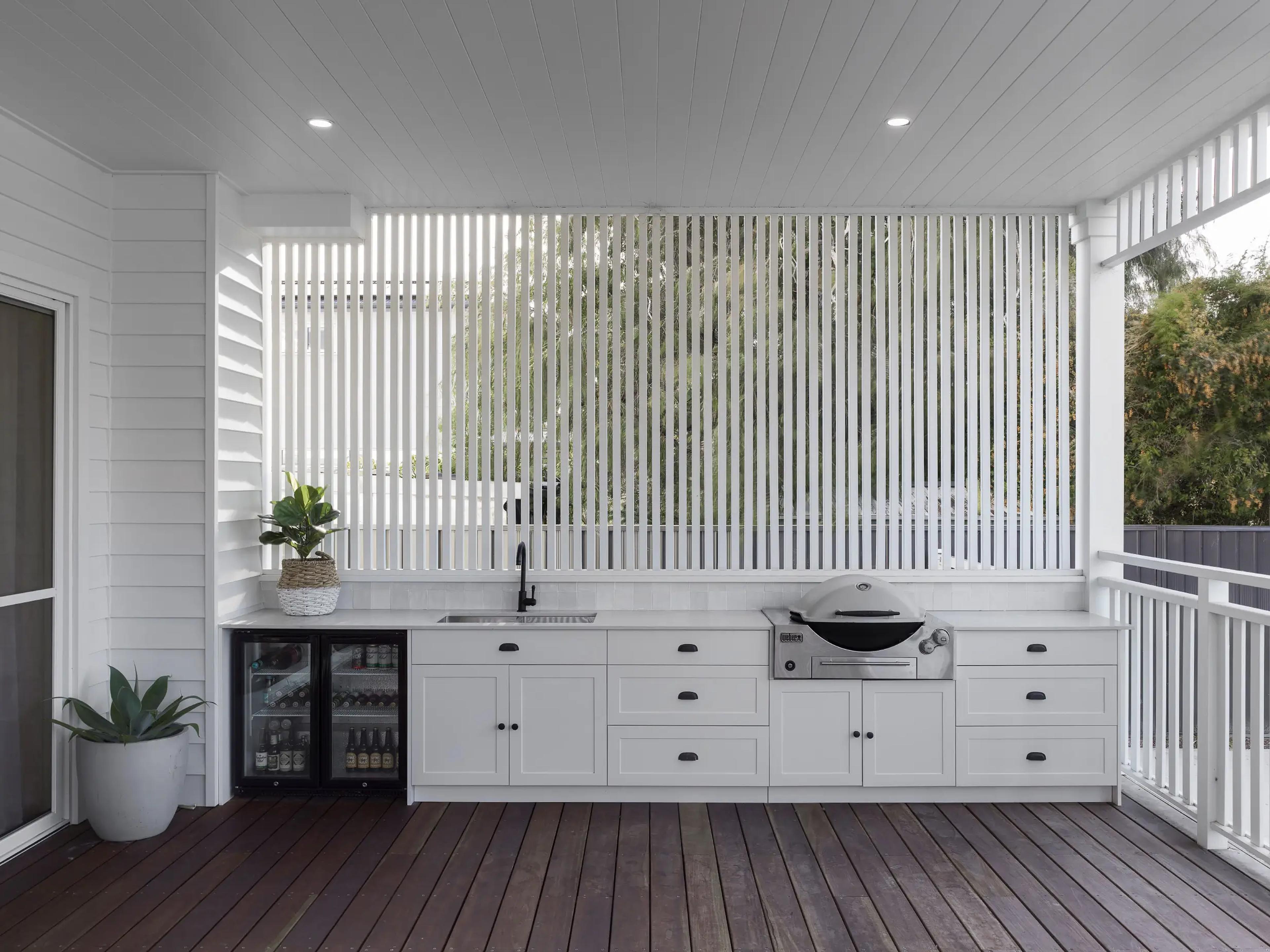 Covered deck with white outdoor kitchen, barbecue and timber floor