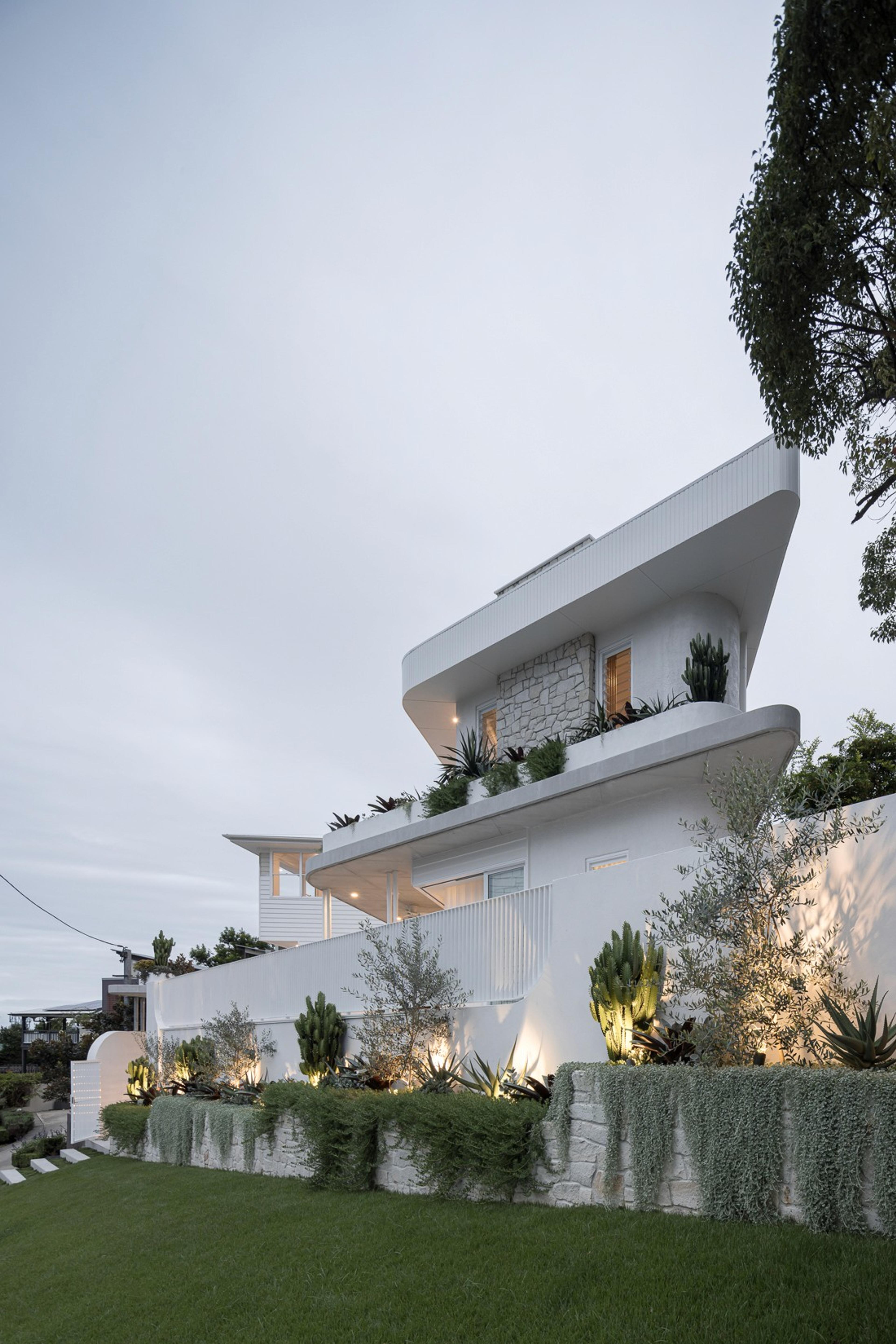 White curved contemporary home above landscaped garden at dusk