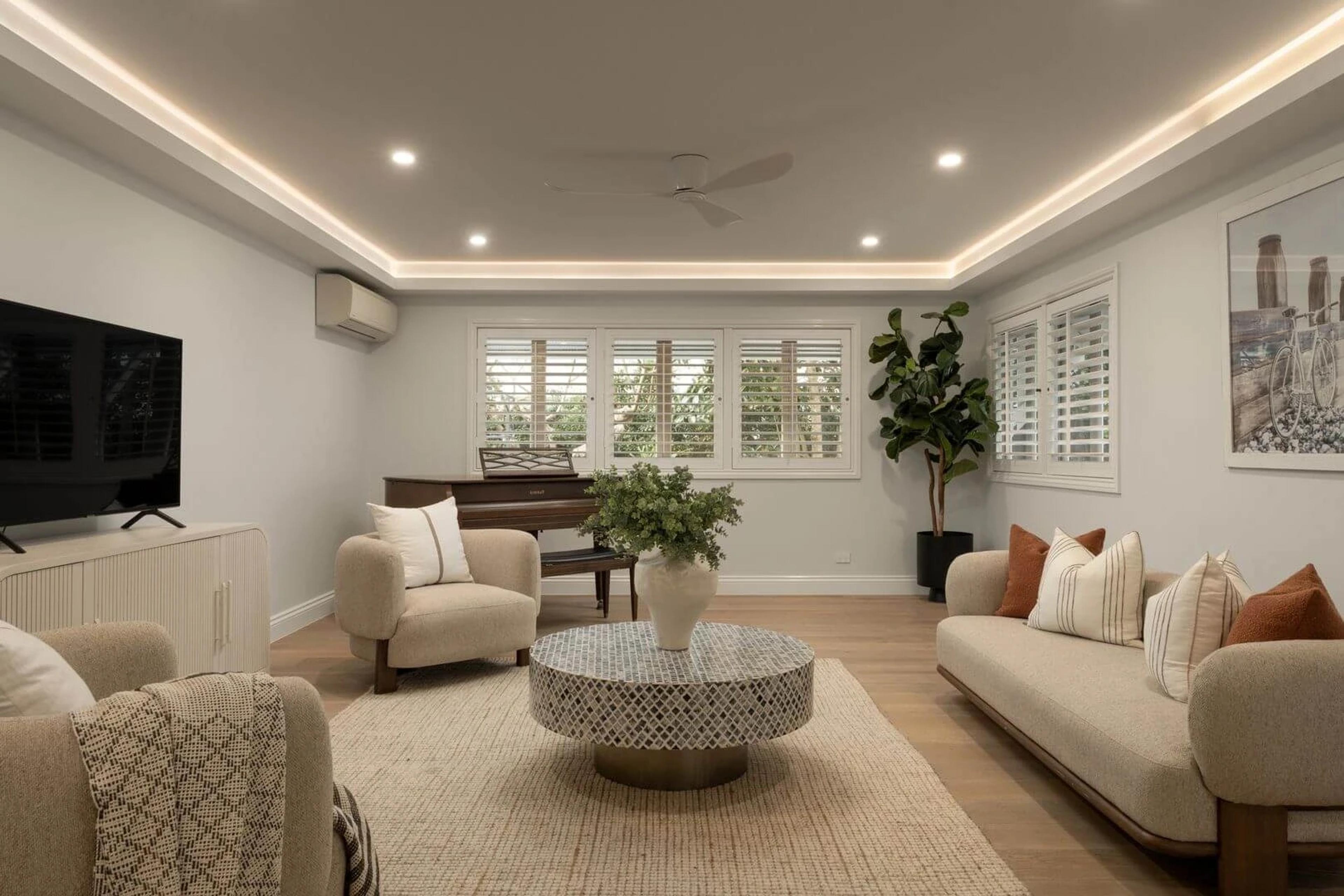 Living room with beige sofas, upright piano and plantation shutters