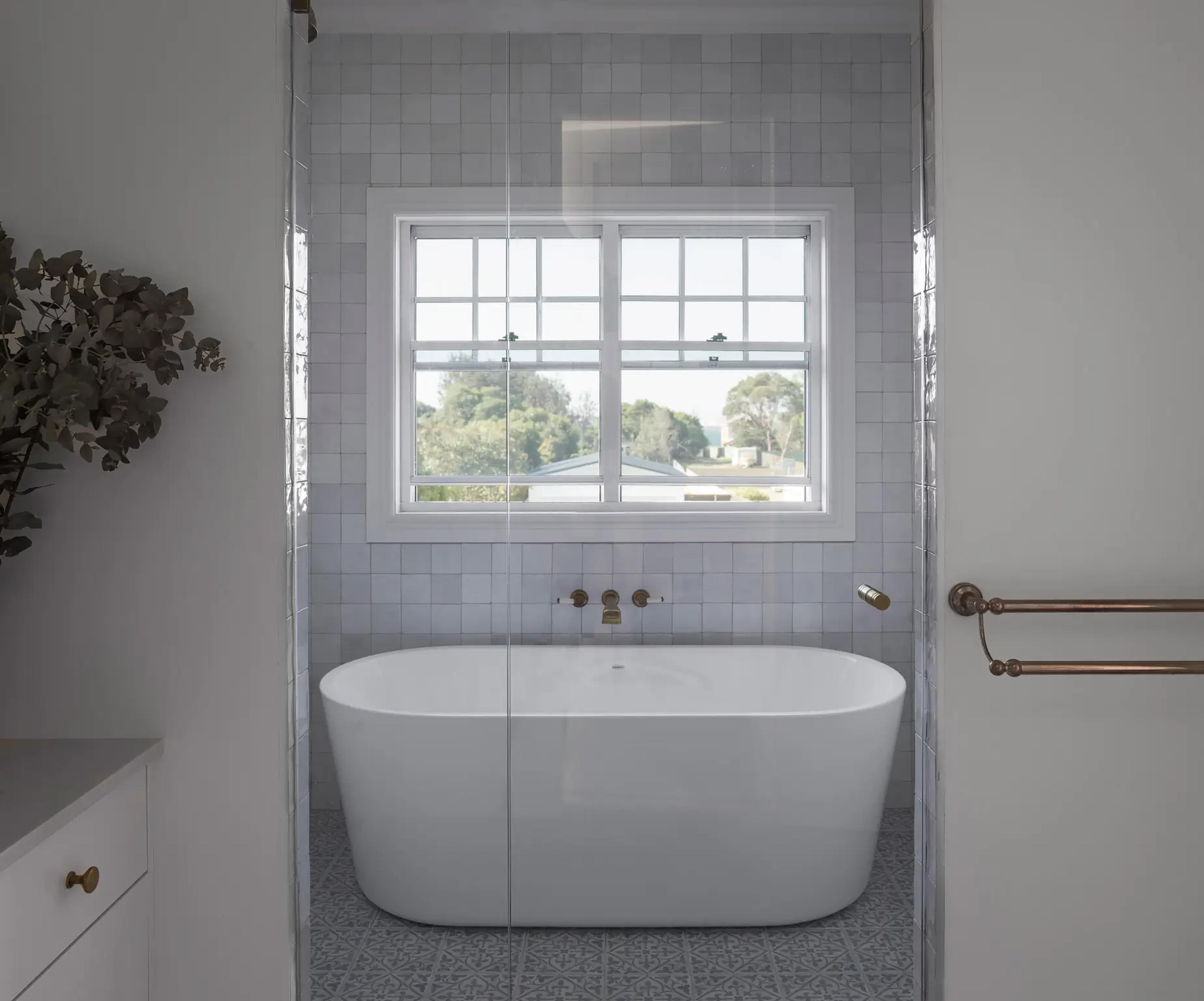 Freestanding bath below a window with garden and water views