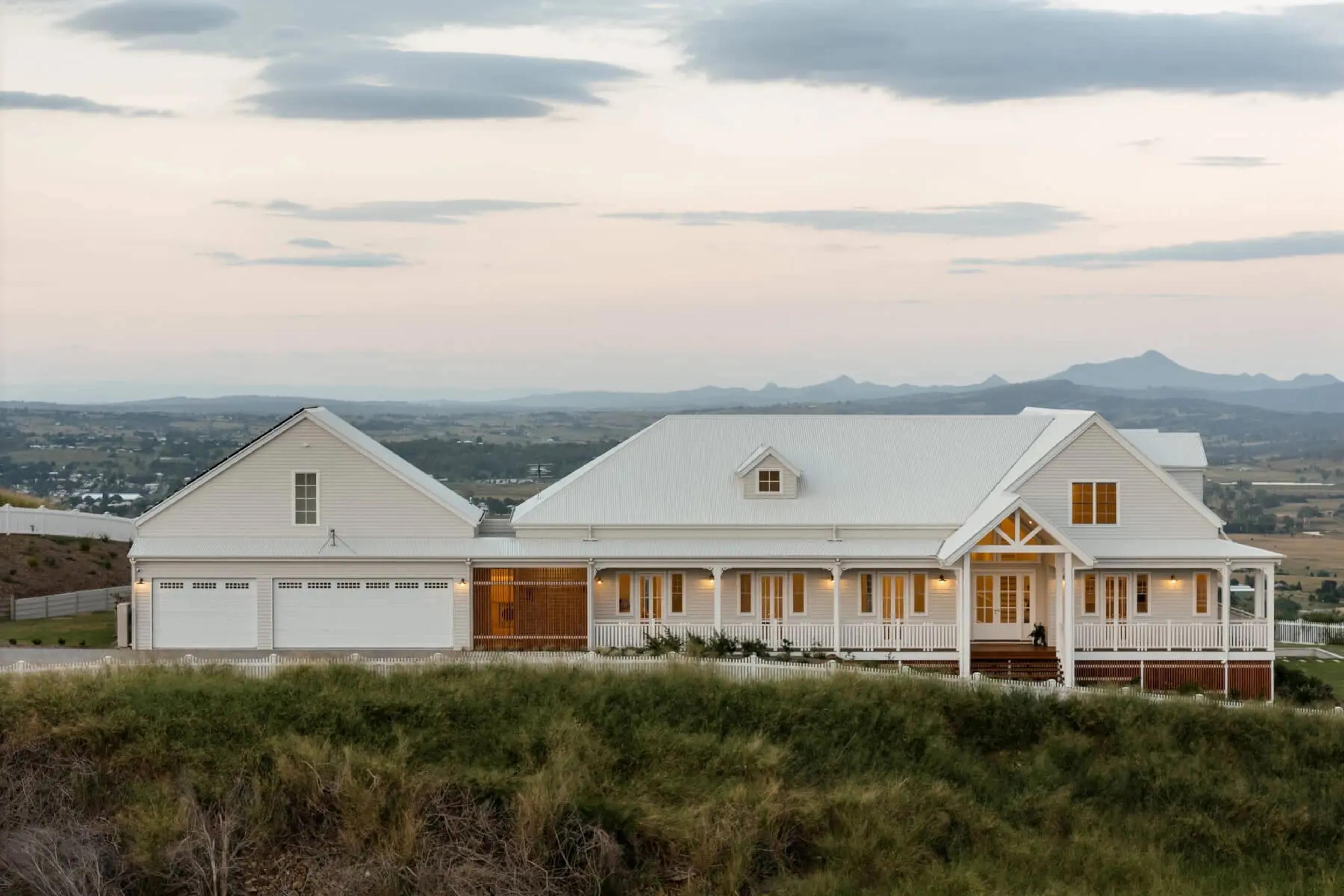 White weatherboard homestead with triple garage at dusk on hilltop