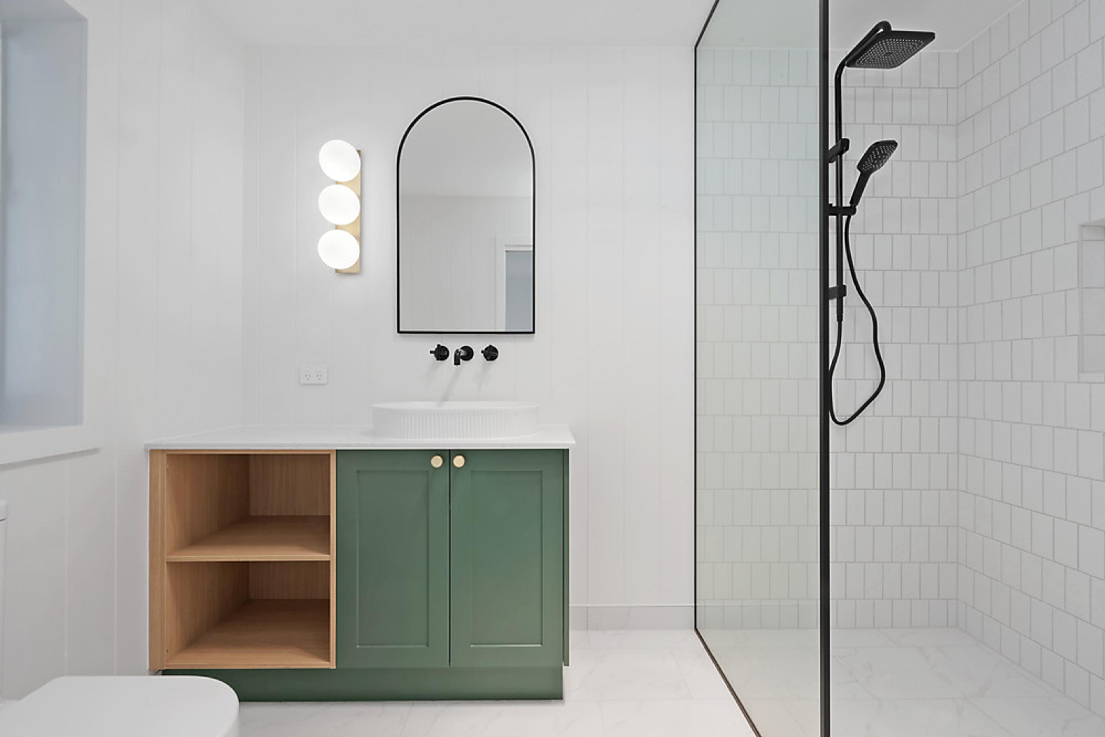 Bathroom with green vanity, open timber shelving, arched mirror and walk-in shower