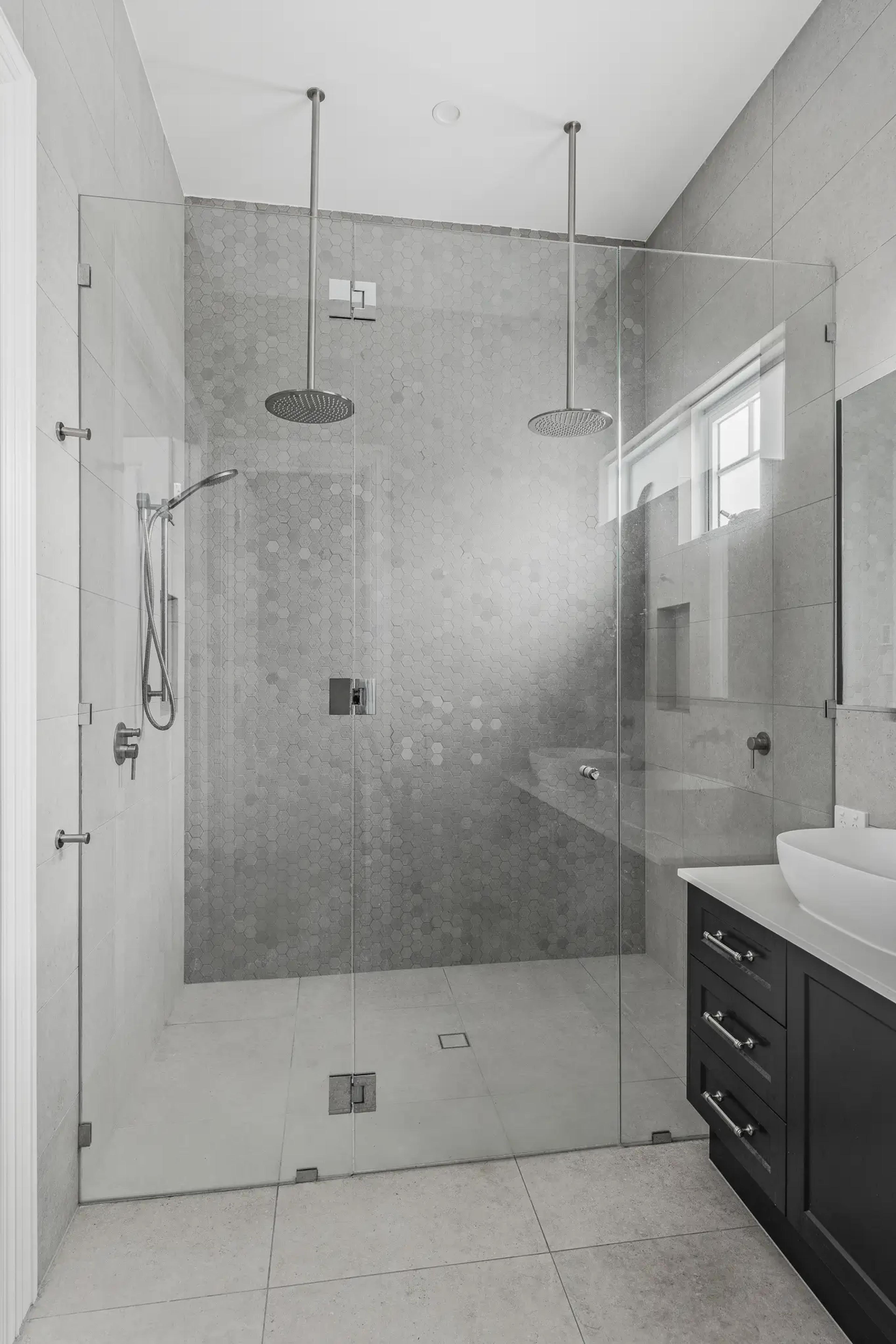 Ensuite with dual rain shower behind glass and grey tiling