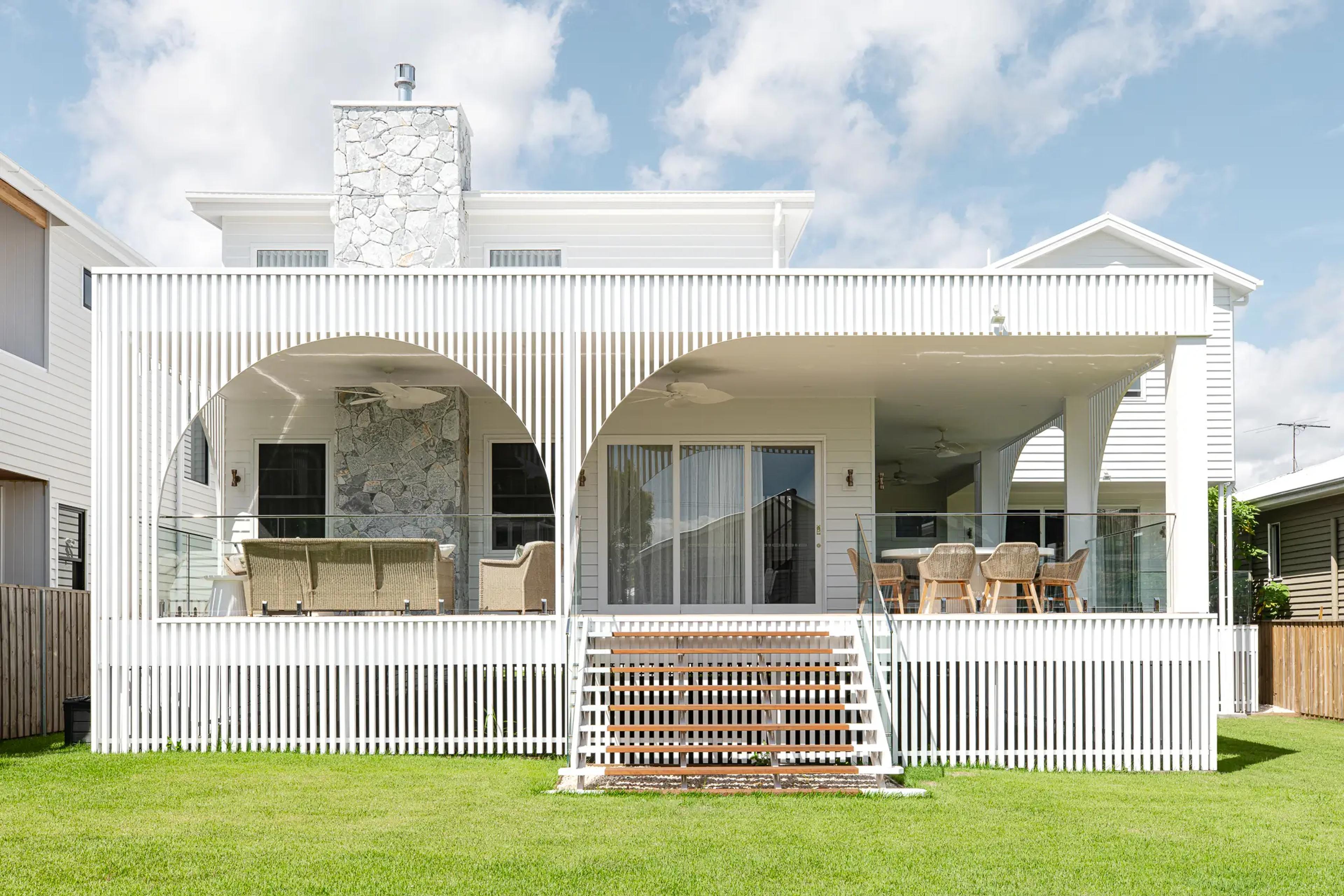 Rear elevation of white home with arched verandah and stone chimney