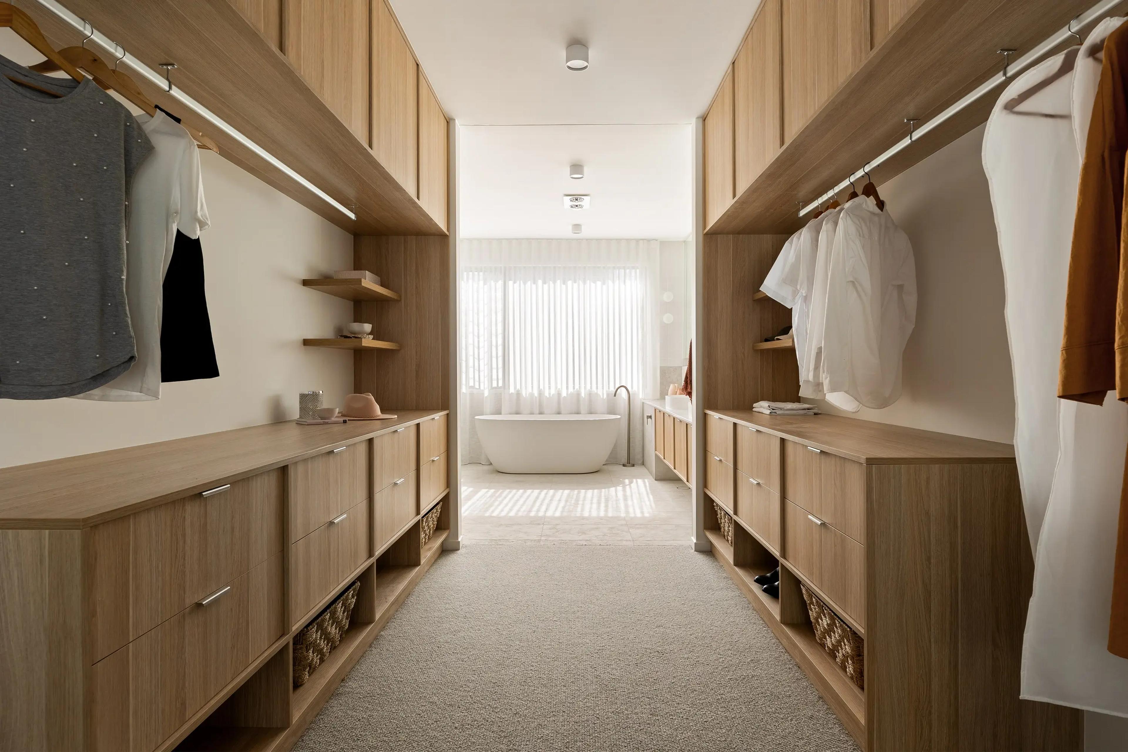Walk in wardrobe with timber joinery leading to freestanding bath