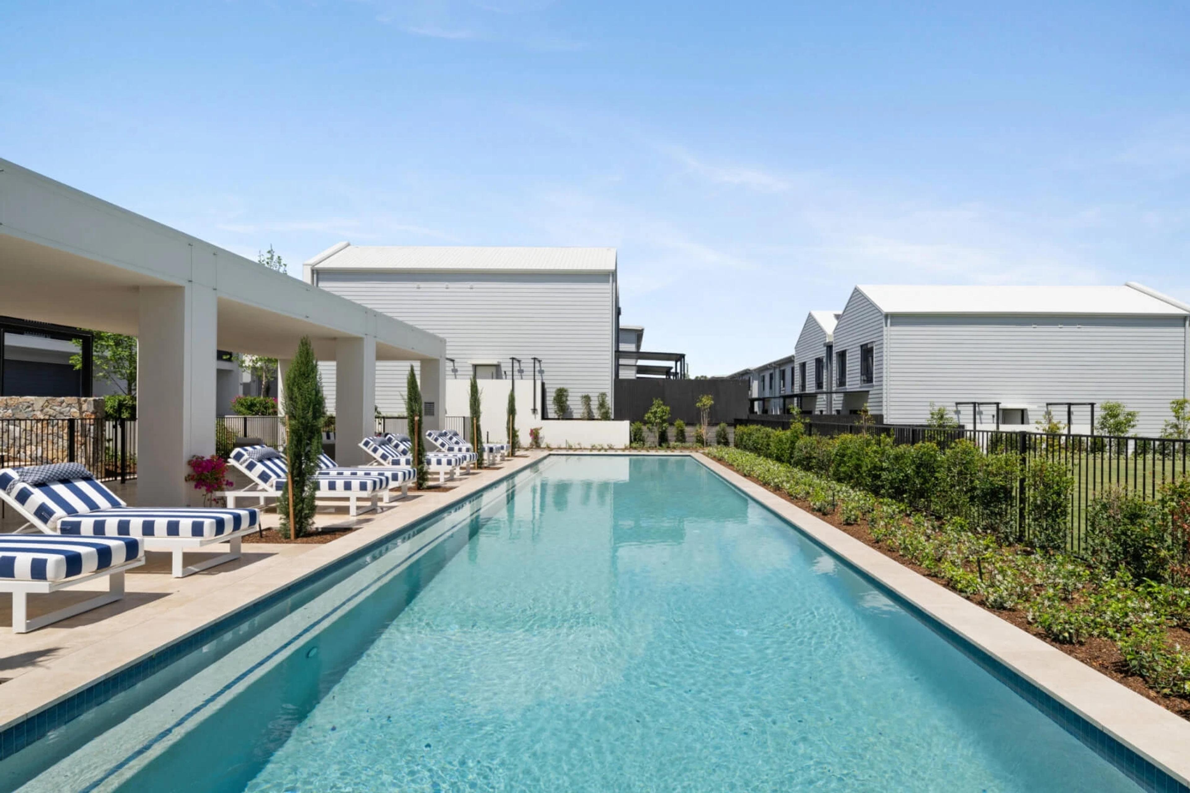Lap pool with sun loungers beside white townhouses