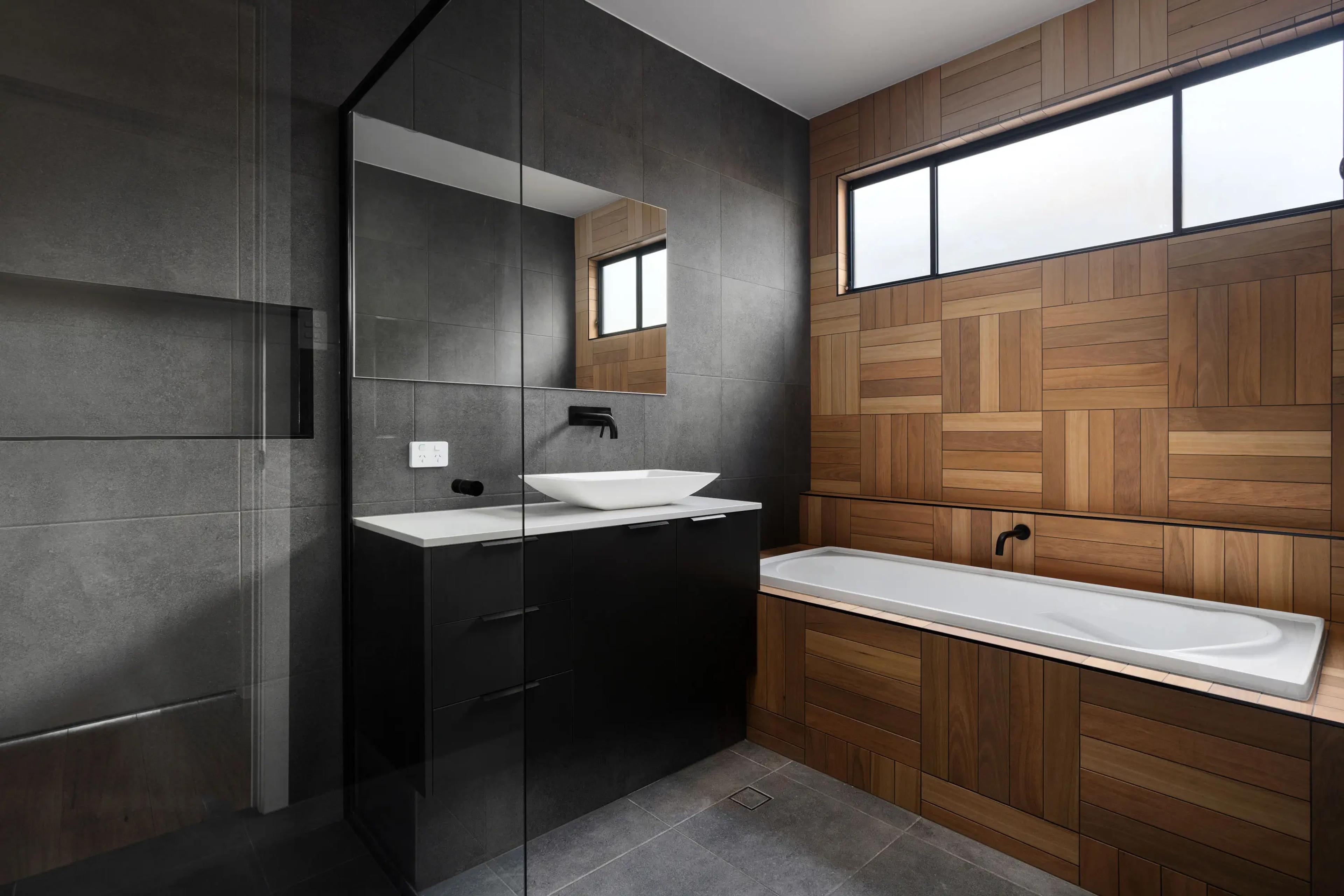 Bathroom with dark tiles, timber wall and inset bathtub