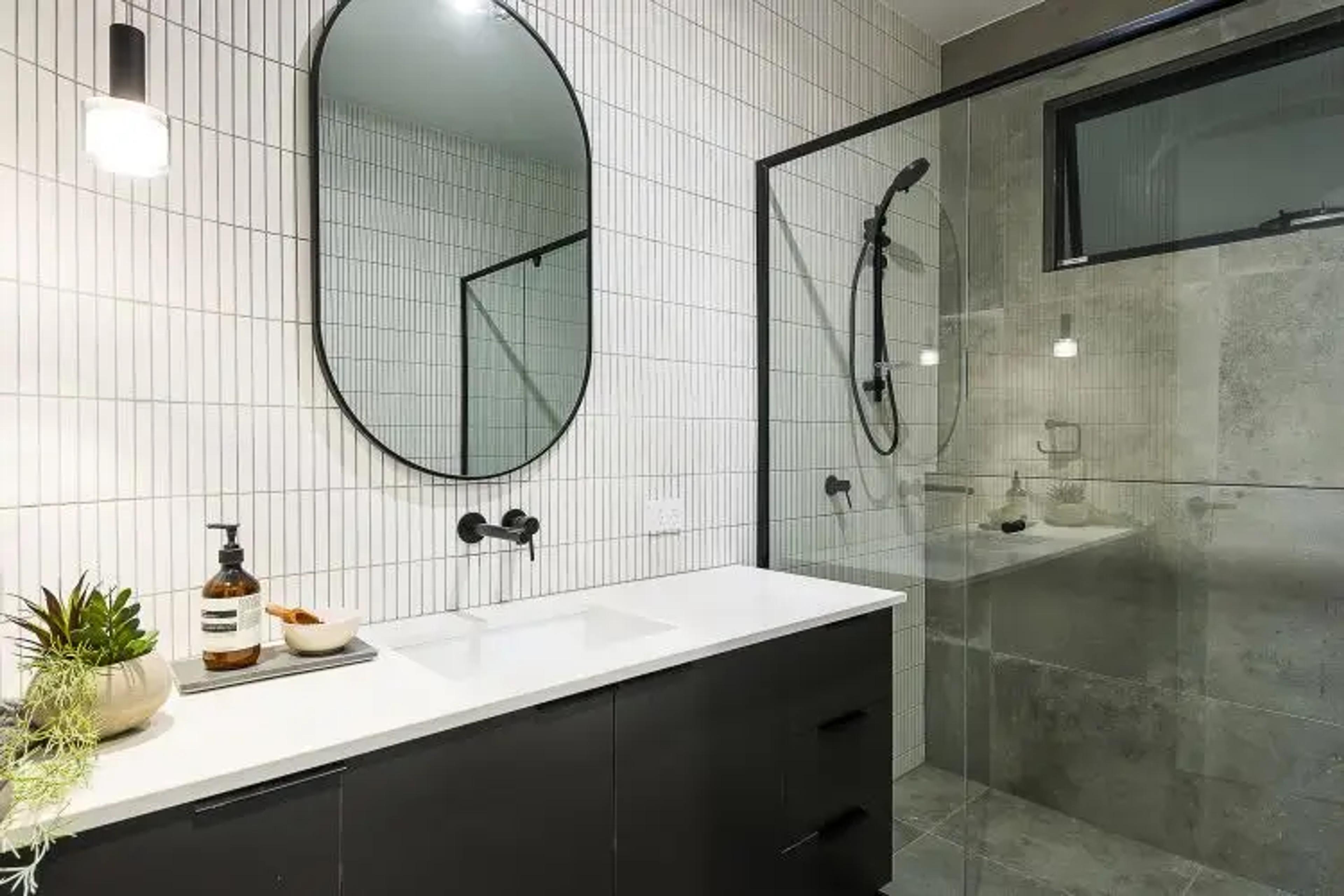 Bathroom vanity with round mirror beside glazed shower